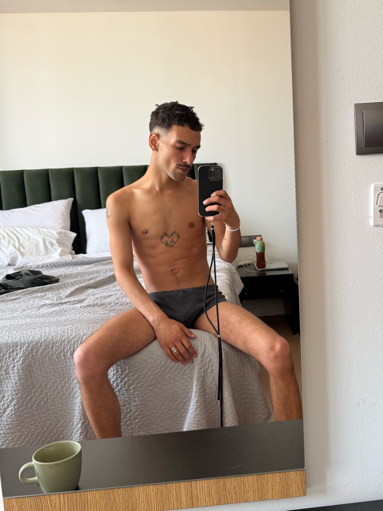 A man takes a mirror selfie in his underwear. He is shirtless, showing off his physique and a small tattoo.