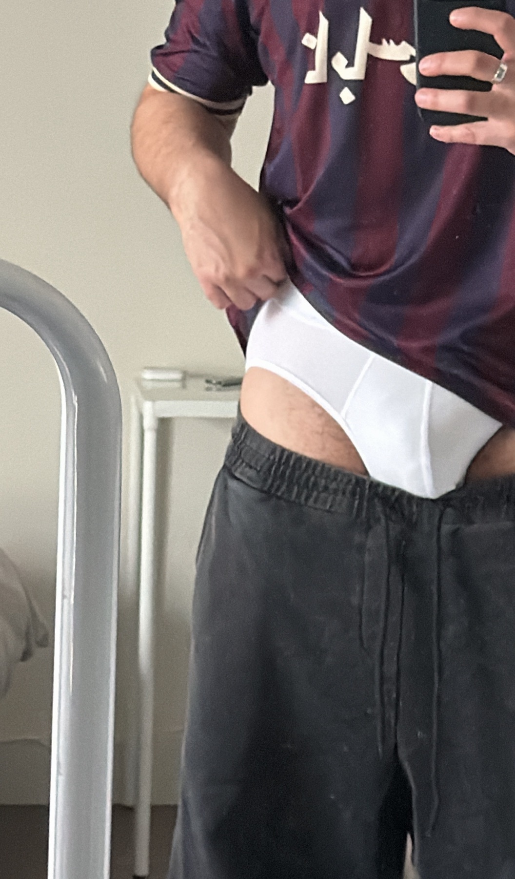 A man is seen in a mirror selfie, pulling up his underwear. He is wearing a jersey and black shorts.