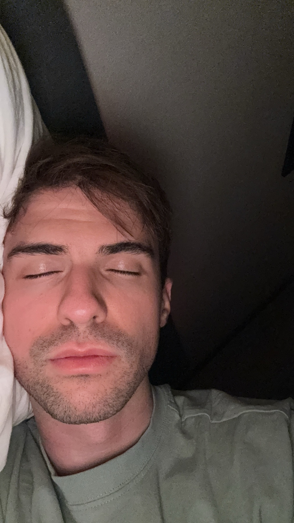 A man is sleeping with his eyes closed. The photo is a selfie.