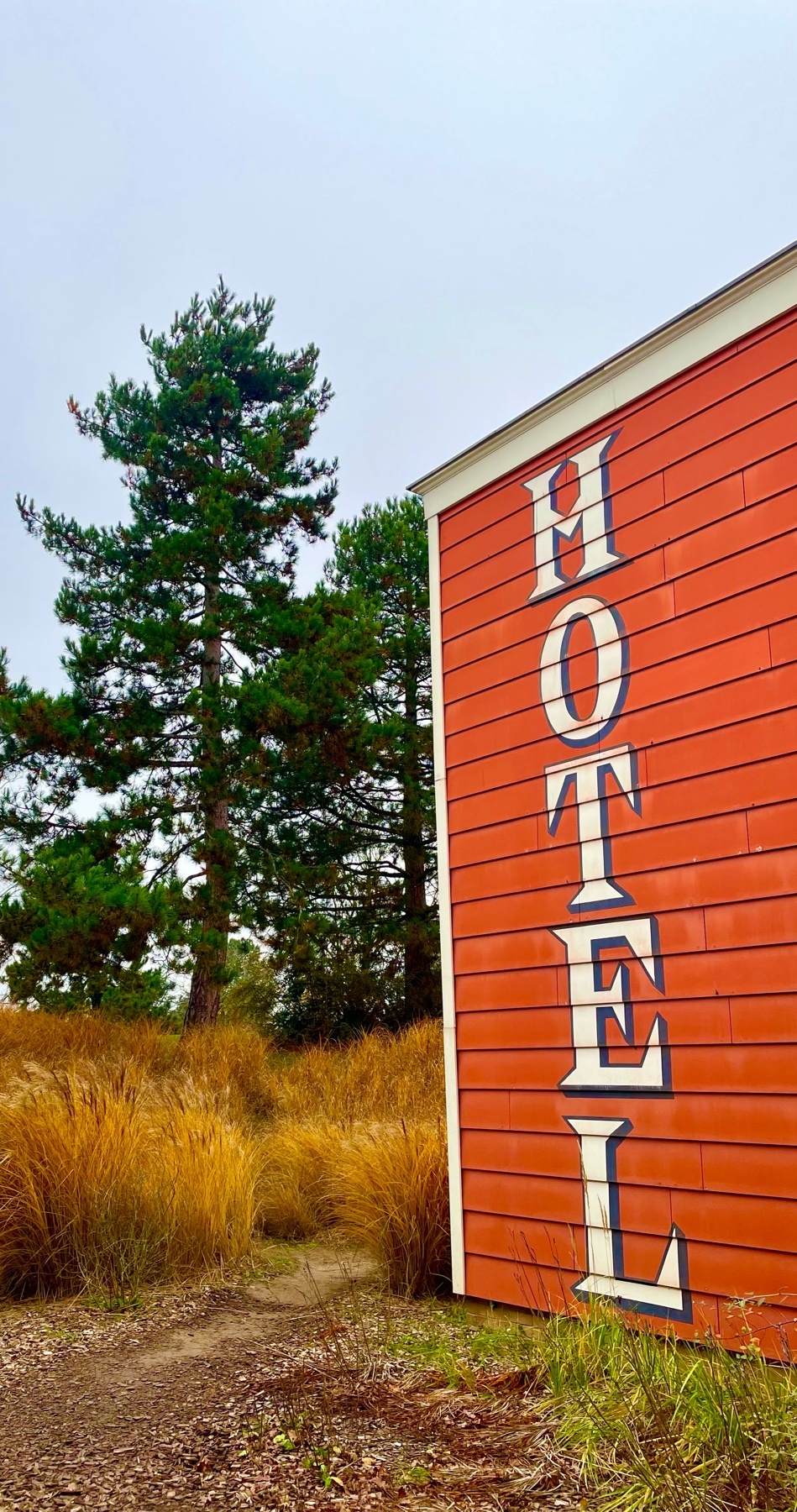 A red hotel sign stands out against a backdrop of trees and tall grass. The image captures a sense of travel and destination.