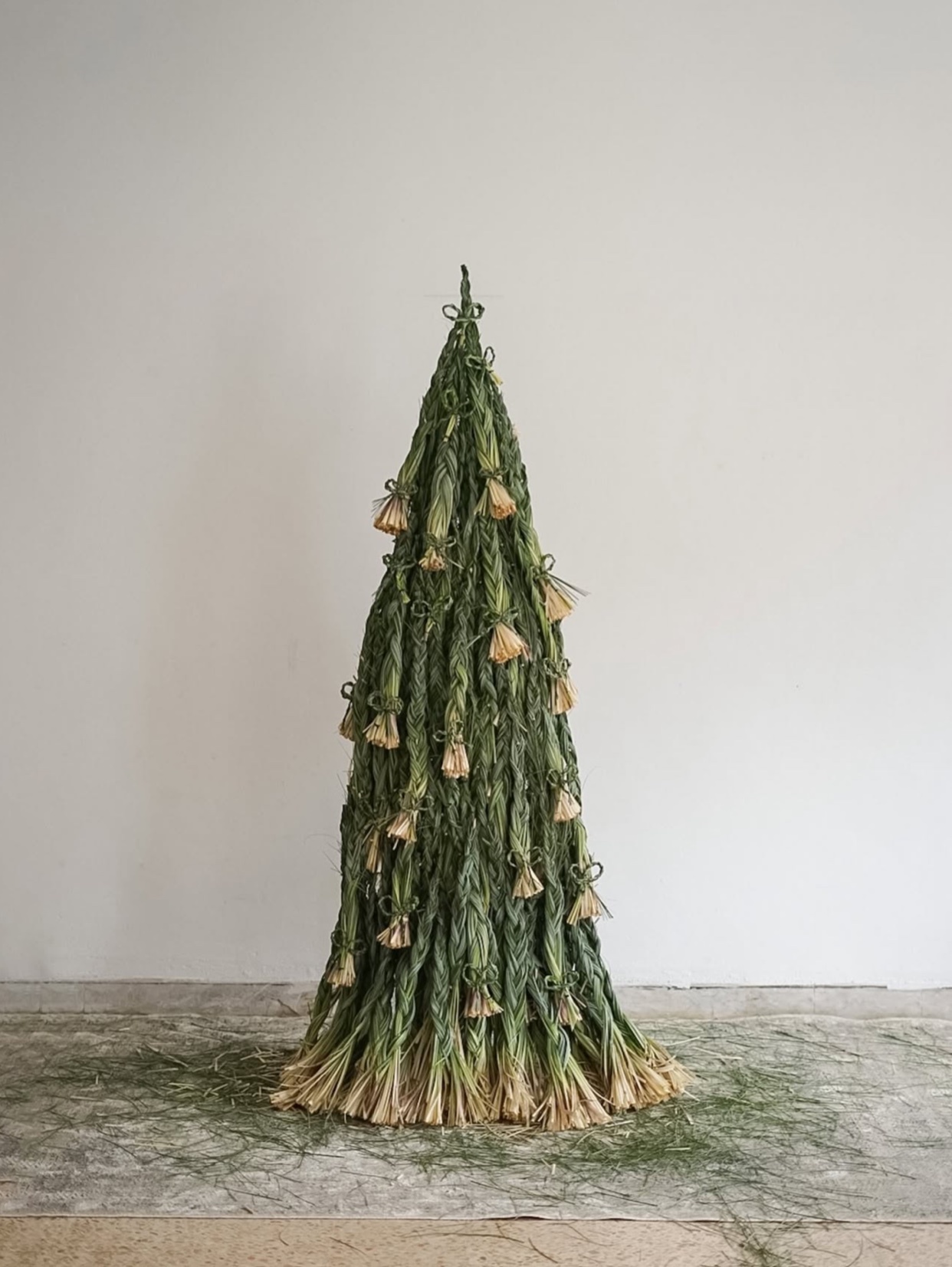 A unique, abstract Christmas tree sculpture made of green and tan materials. The tree stands tall against a plain white background.
