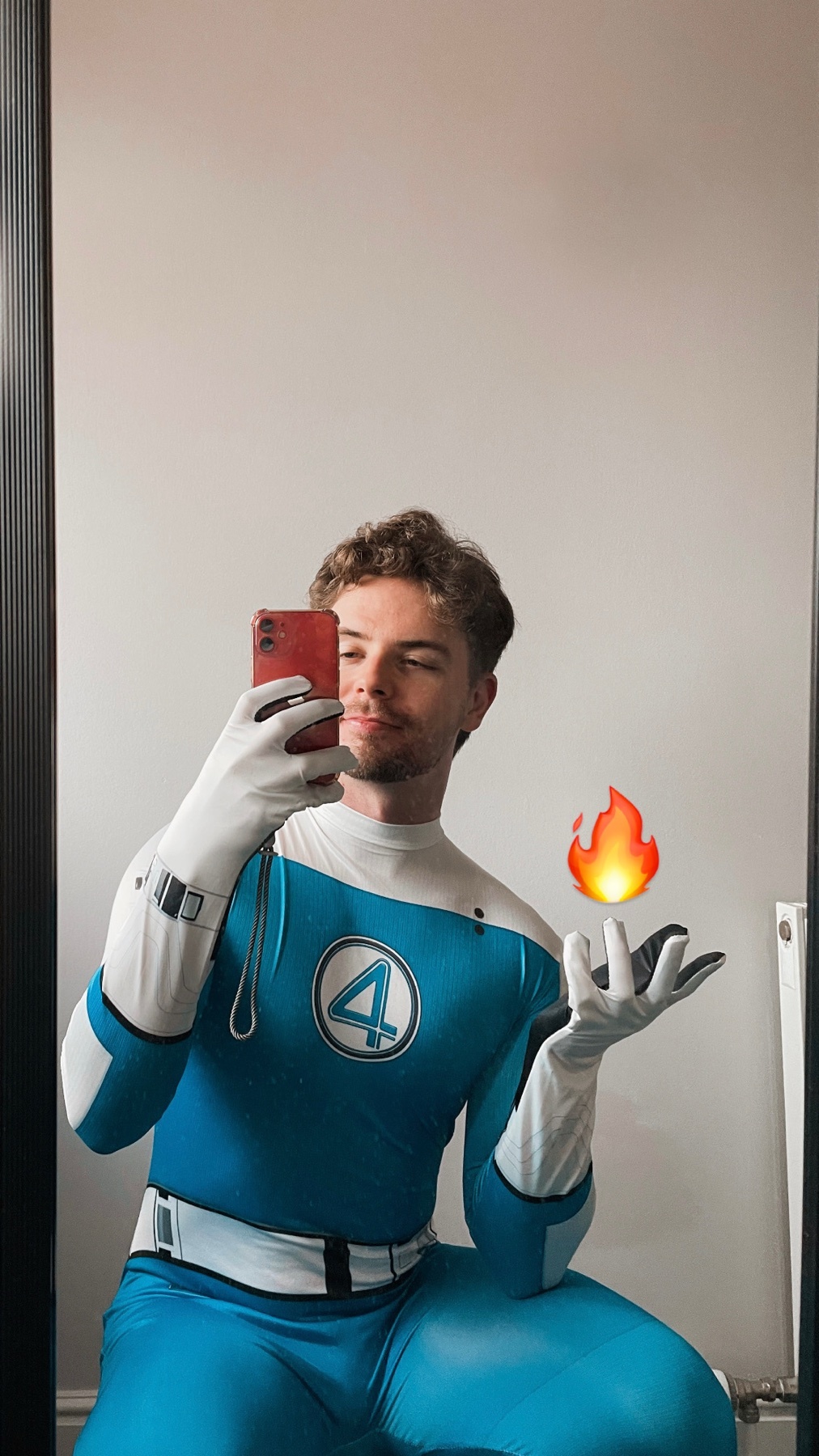 A man in a Fantastic Four costume takes a selfie. He is holding a flame emoji in his hand.
