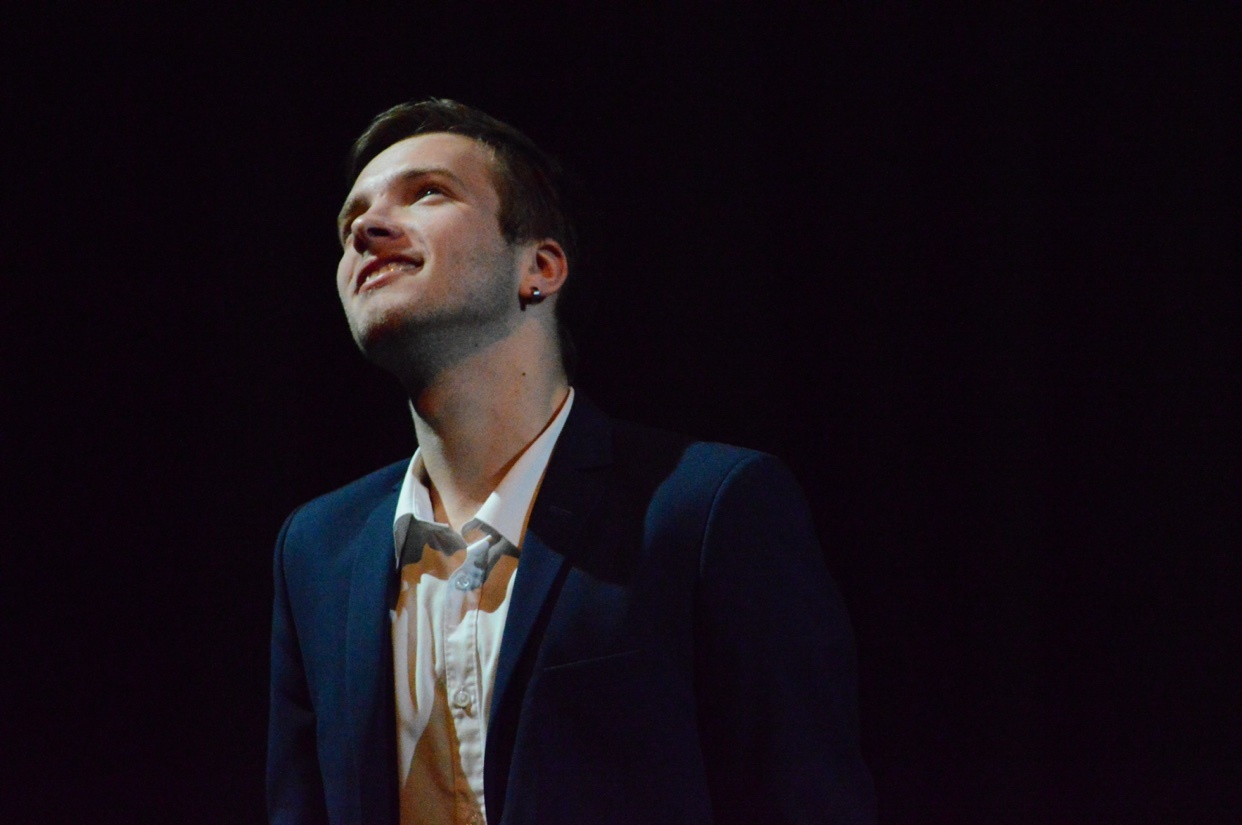A man in a suit and tie looks up and smiles against a dark background.