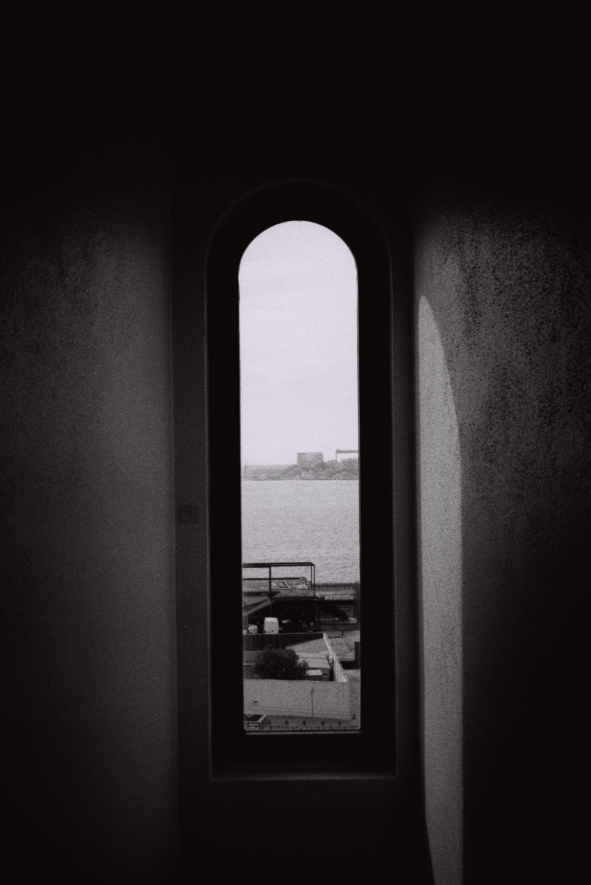 A black and white photo of a window with an arched top, offering a view of a cityscape. The minimalist design and play of light and shadow create an artistic aesthetic.