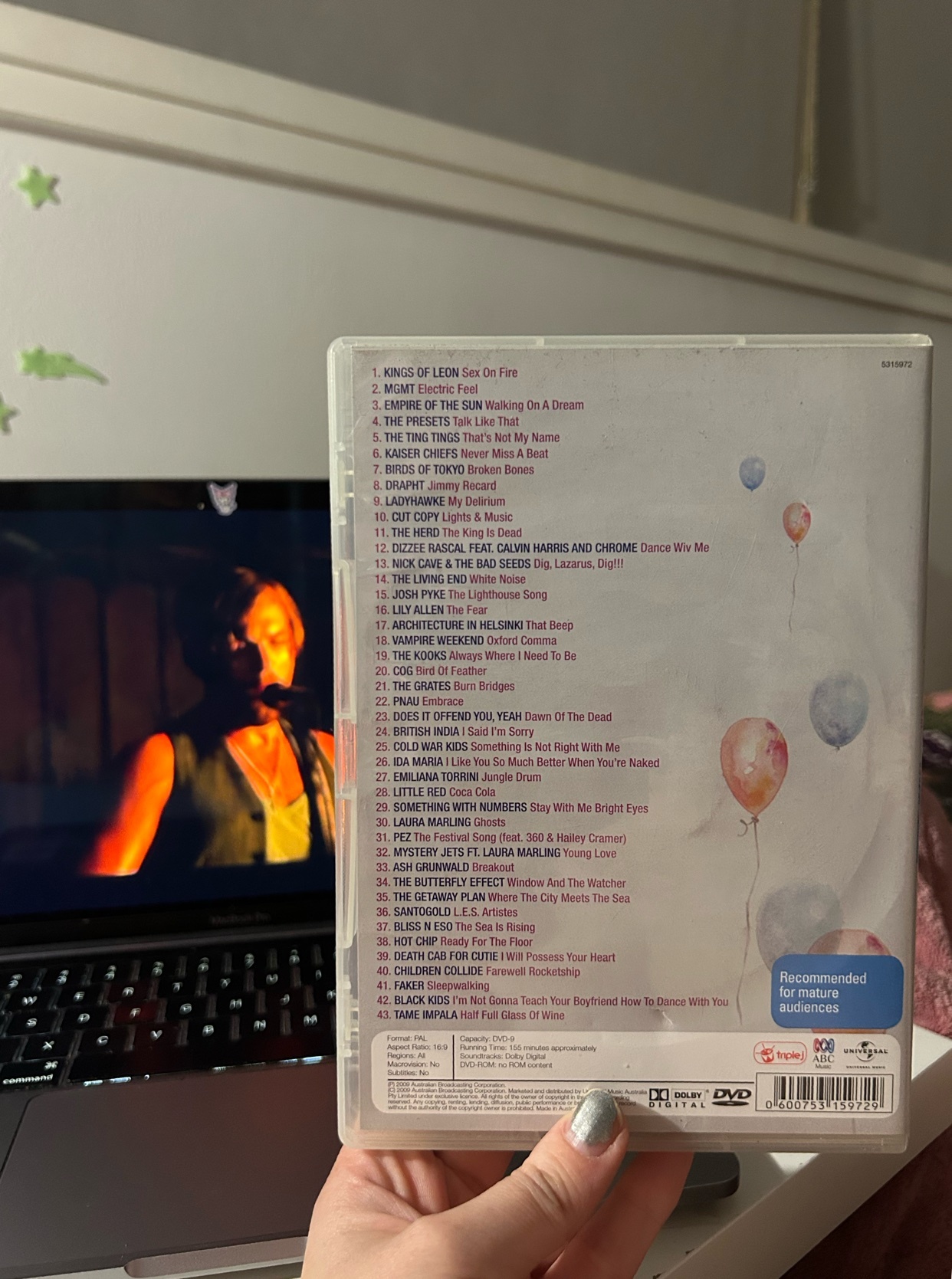 A DVD case with a list of songs from the 2008 Triple J Hottest 100, with a laptop screen showing a music video in the background.