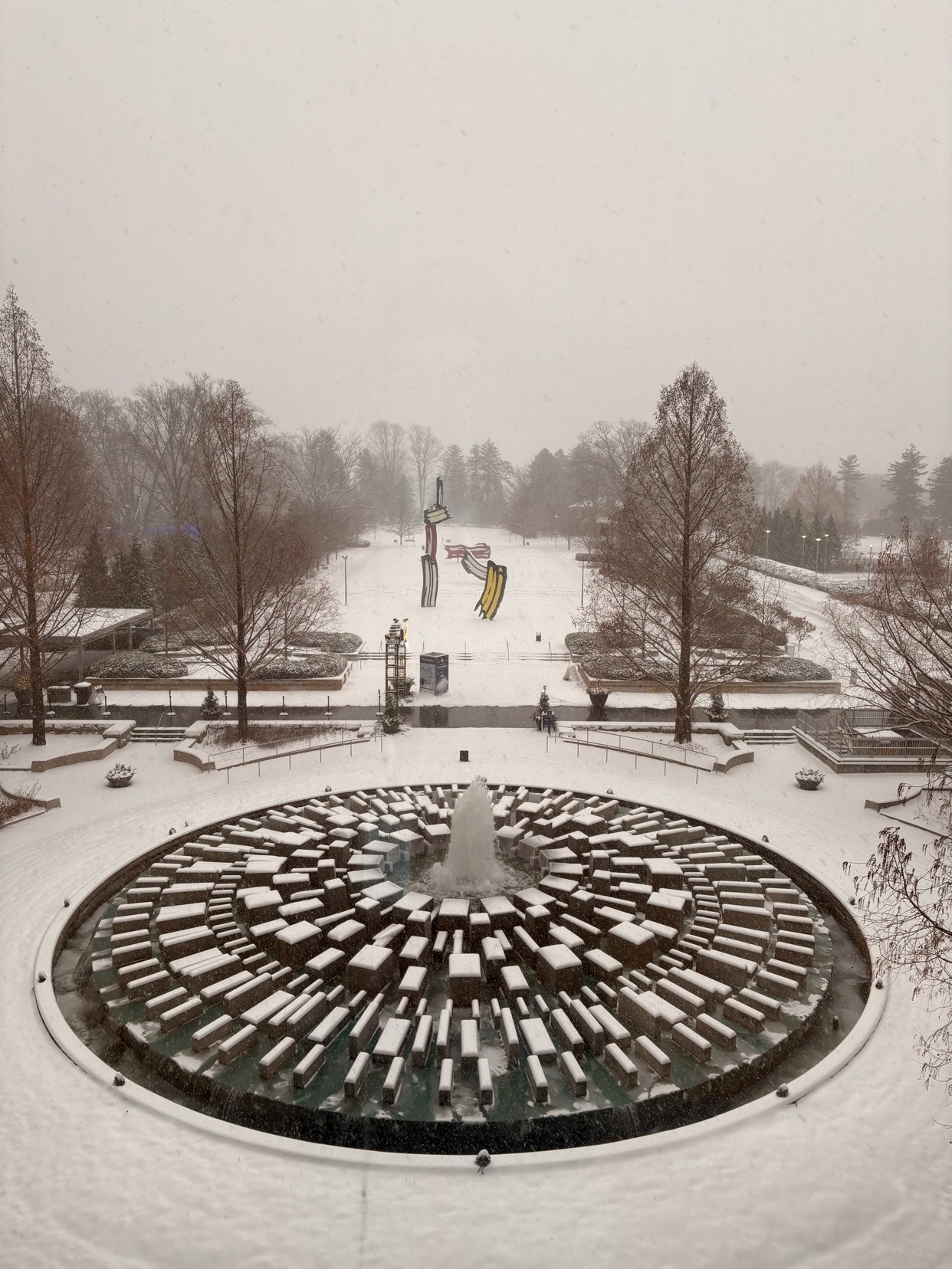 A snow-covered park with a unique fountain design. The photo captures a winter landscape with architectural elements.