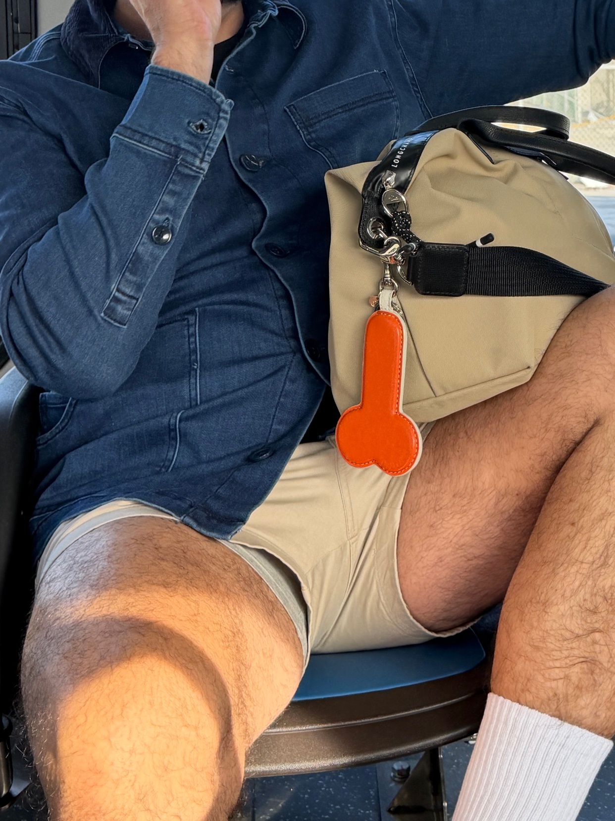 A man is seen wearing a denim shirt and shorts, with a bag and an orange accessory. The photo is suggestive.