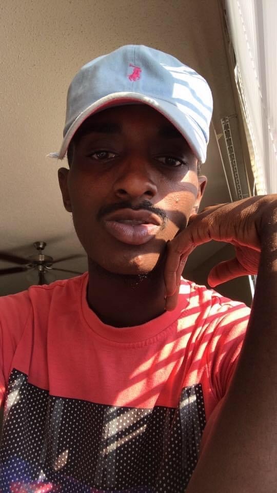 A man takes a selfie, wearing a cap and t-shirt. The man is shirtless.