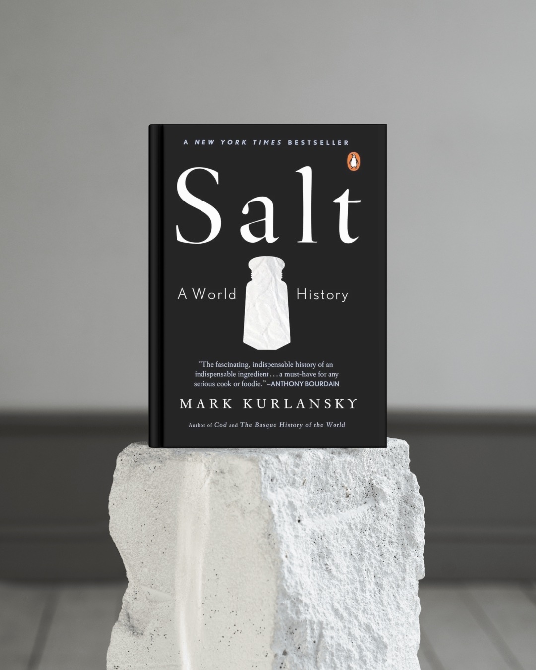 A book titled "Salt: A World History" by Mark Kurlansky is displayed on a textured white pedestal against a neutral gray background.