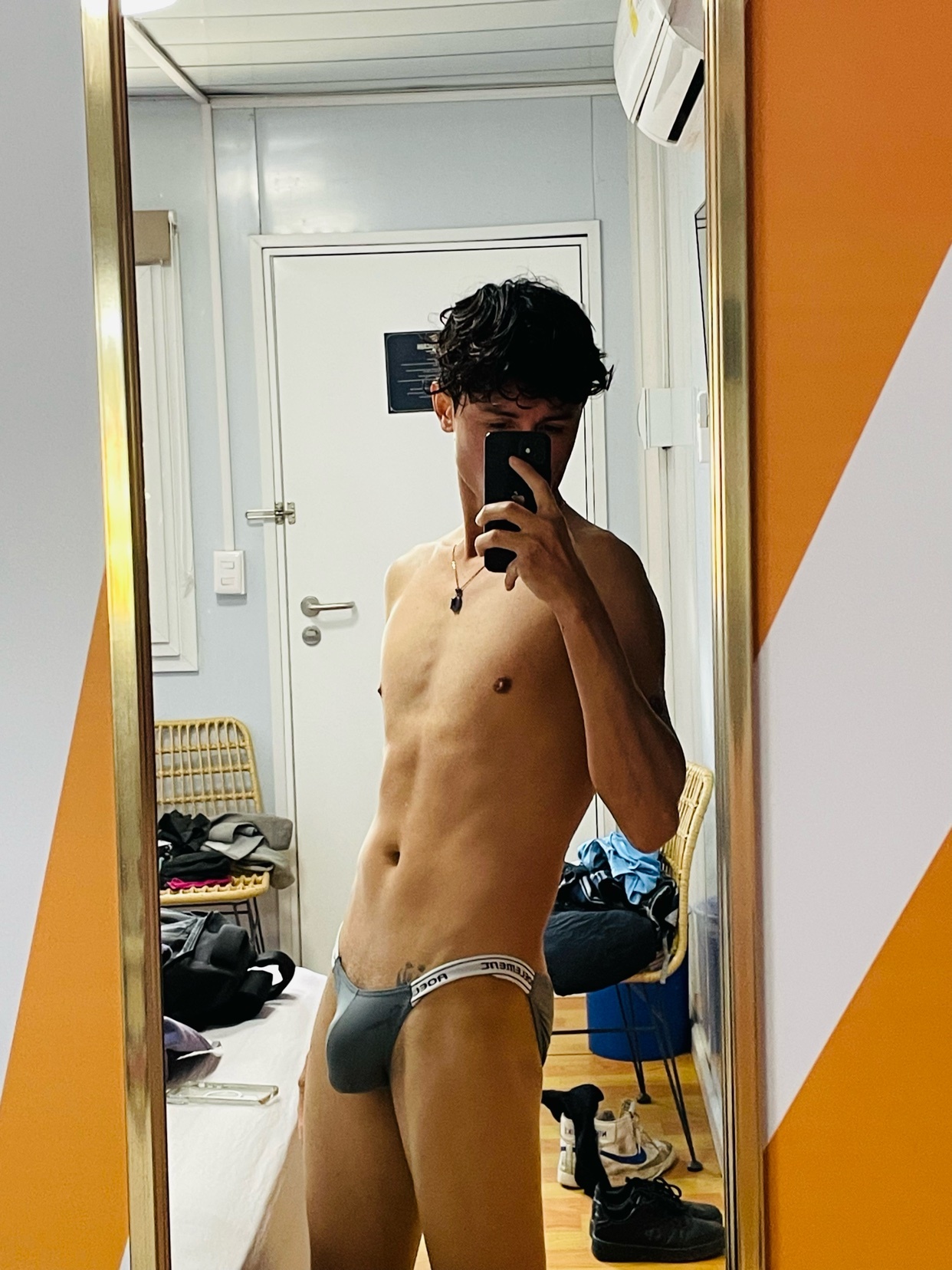 A man takes a mirror selfie, shirtless and wearing underwear. The photo highlights his physique and the interior of the room.