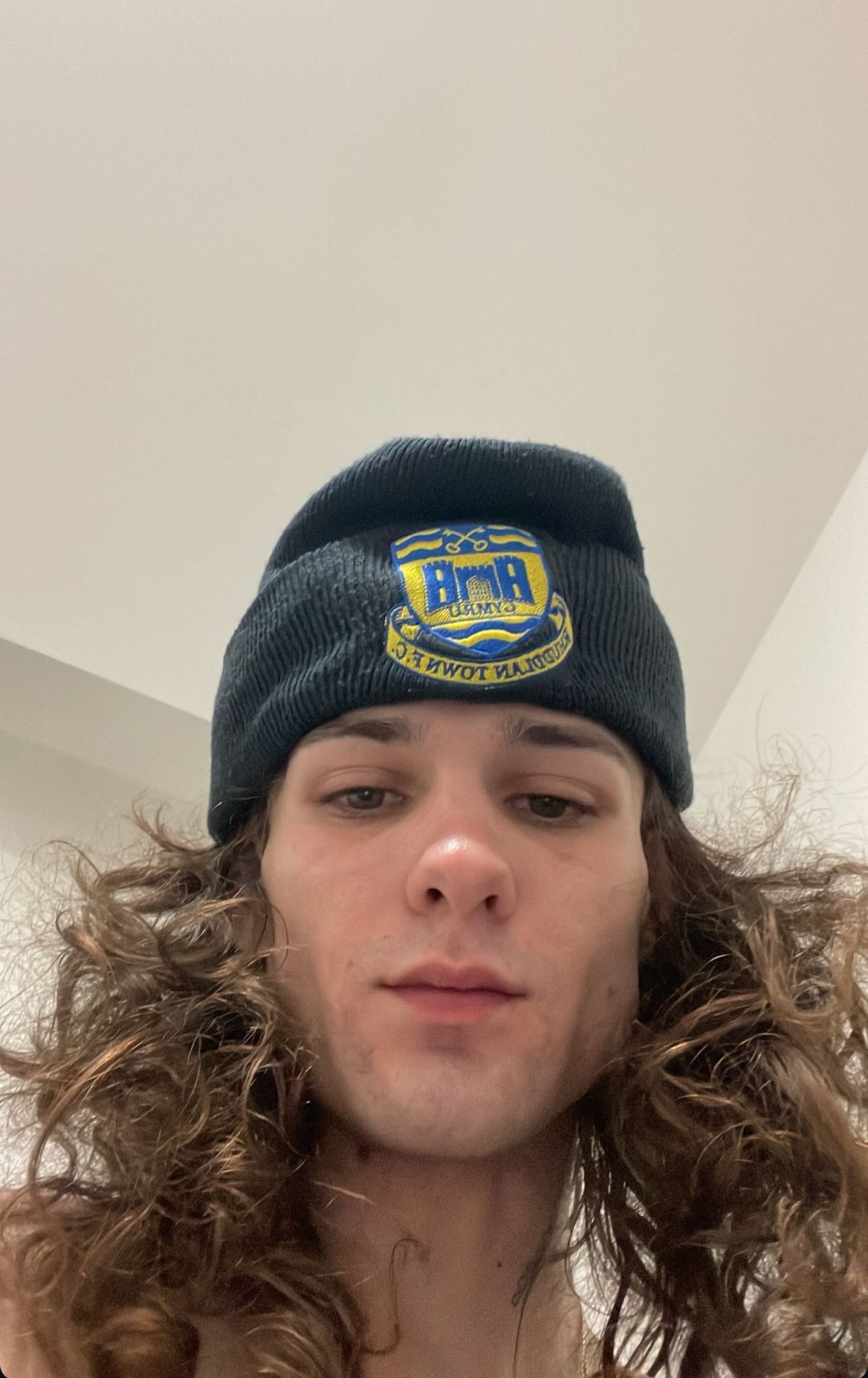 A selfie of a young man with long, curly hair wearing a beanie.