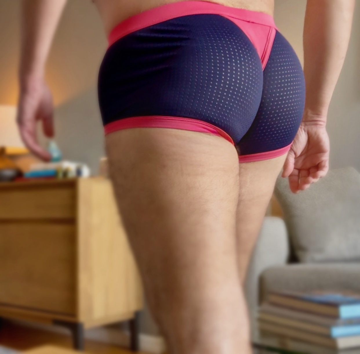 A close-up, rear-view shot of a man's buttocks and upper thighs, wearing dark blue and pink athletic underwear. The underwear has a textured pattern on the back and pink trim.