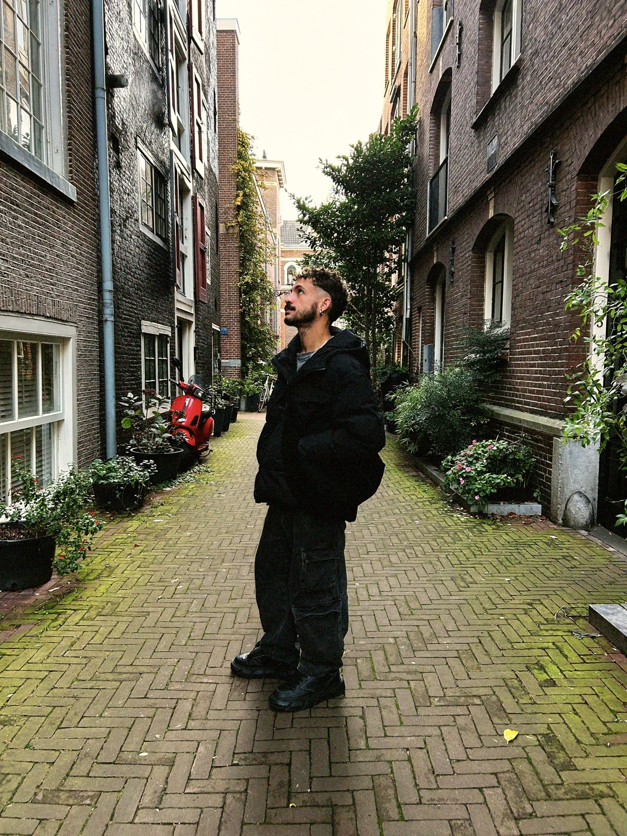 A man stands in an alleyway, looking up. The photo captures the urban landscape with buildings on either side.