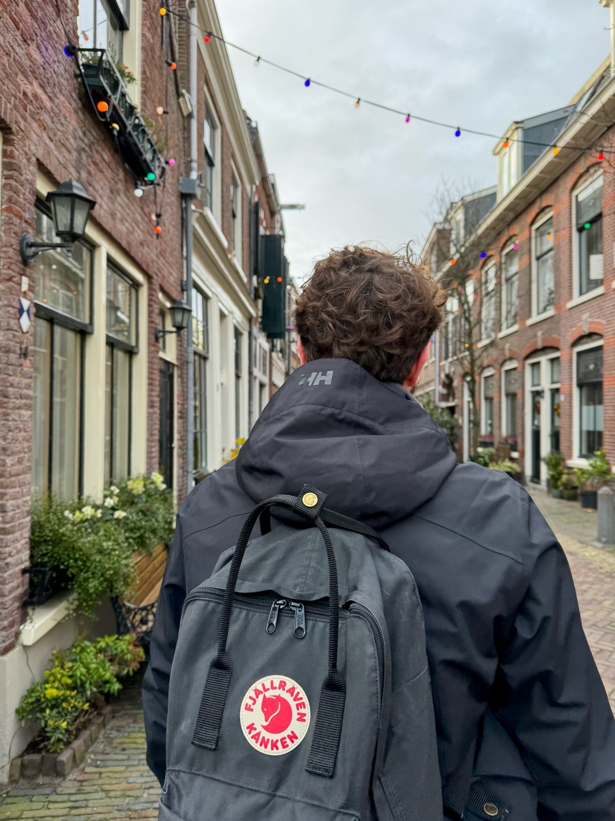 A man walks down a brick-lined street, wearing a jacket and carrying a backpack. The photo captures a moment of urban exploration.