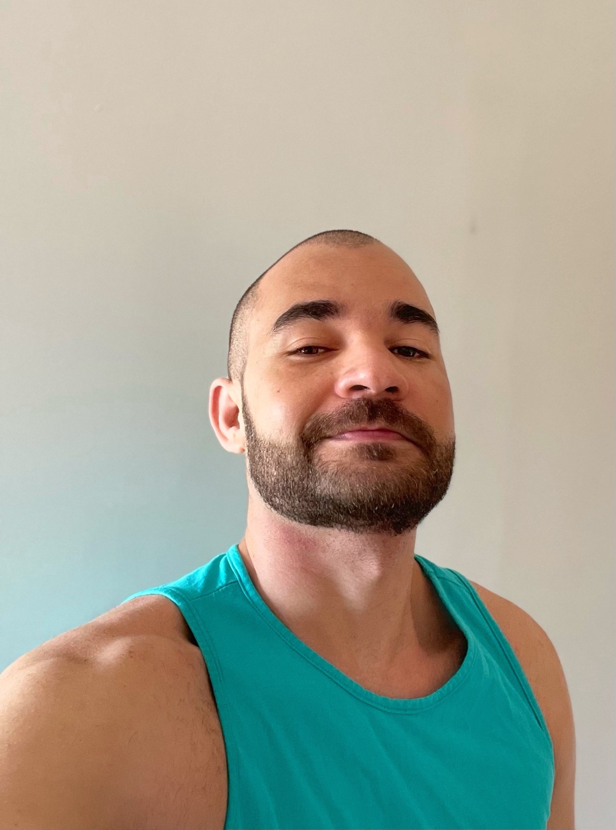 A man with a beard and short hair takes a selfie in a teal tank top.