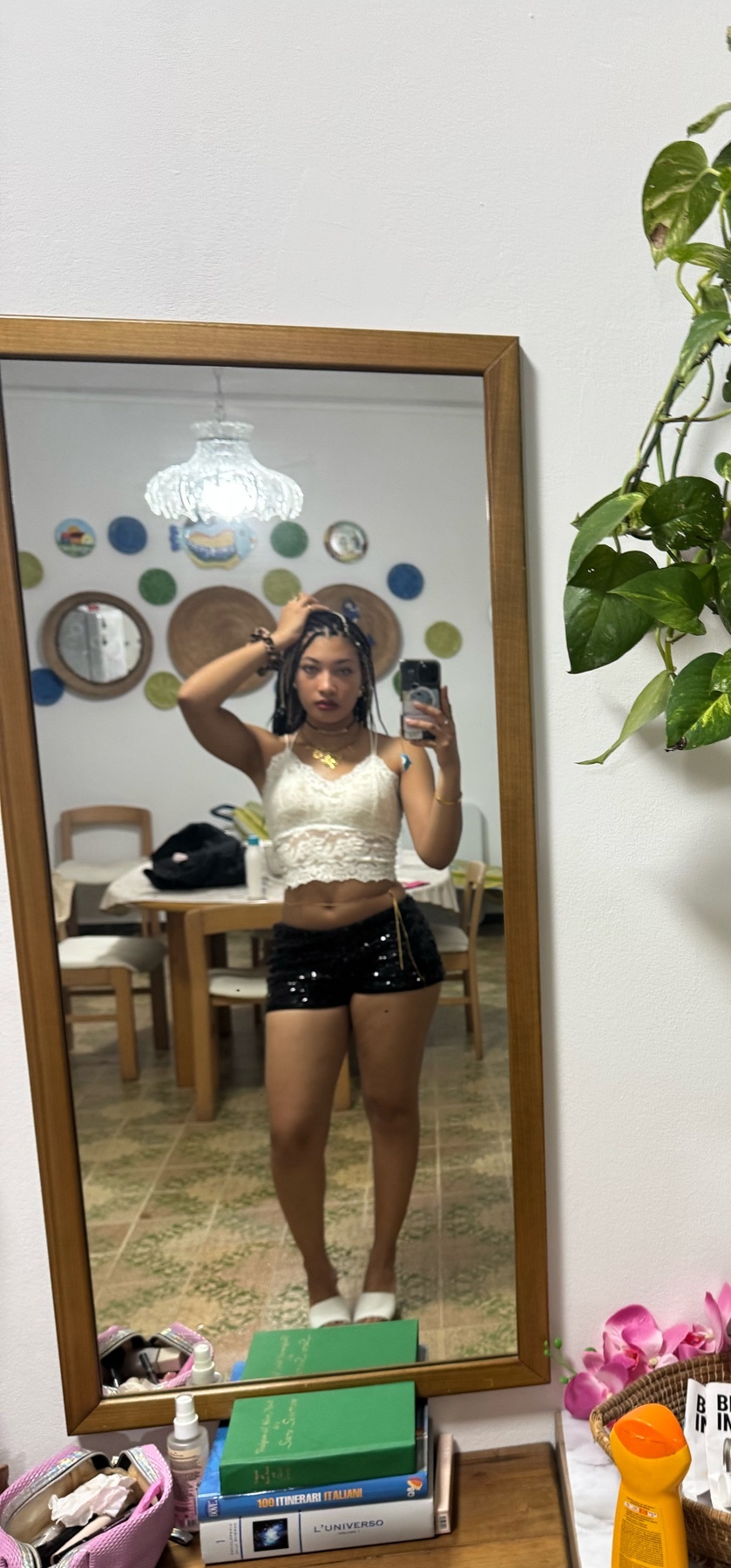 A woman takes a mirror selfie indoors, posing in a white lace crop top and black sparkly shorts.