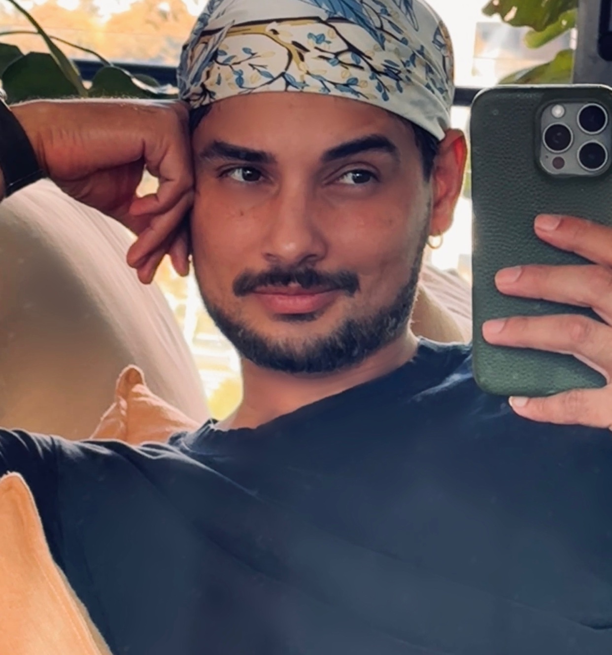 A man takes a selfie in a mirror. He is wearing a bandana and a dark shirt.