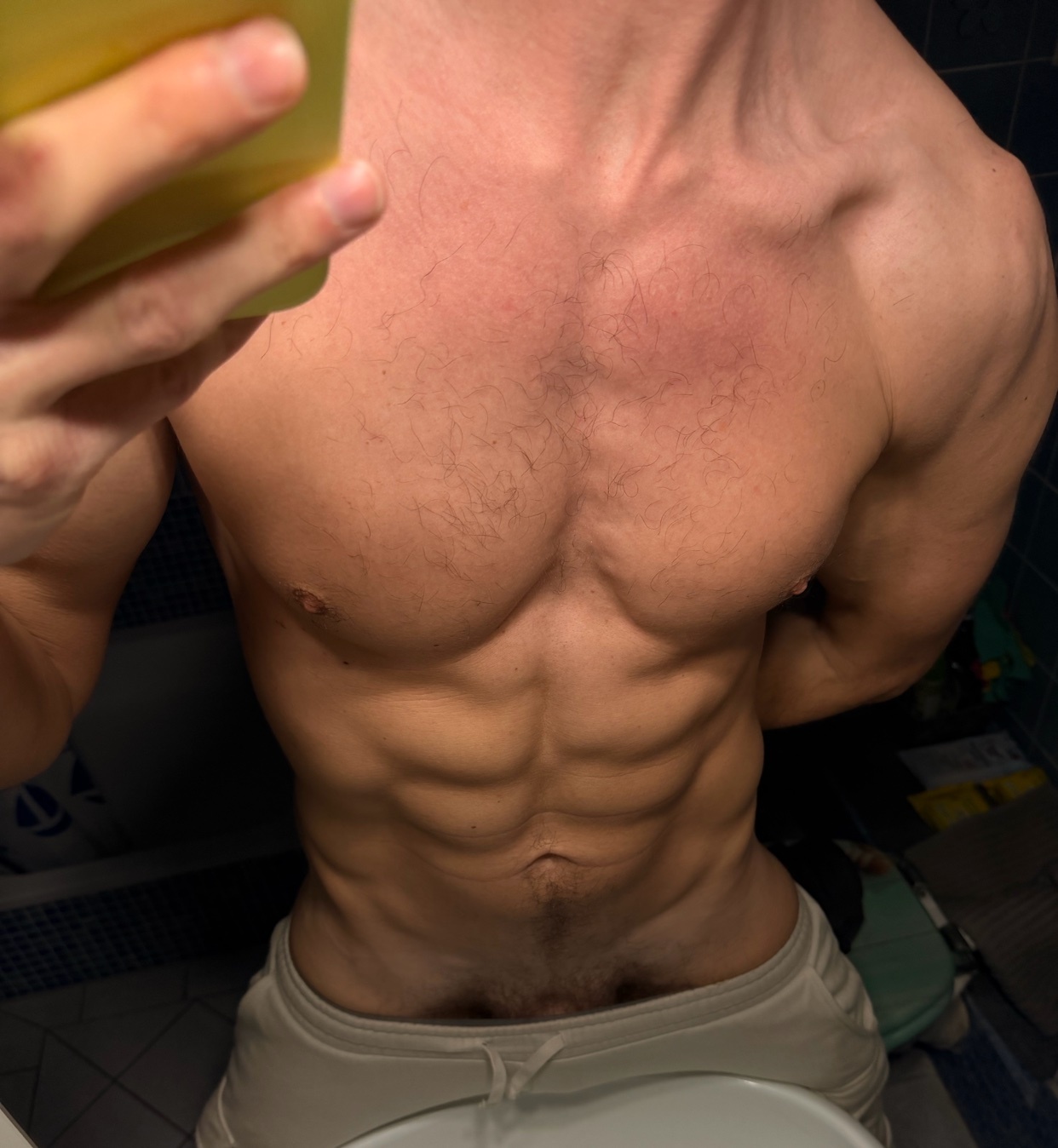 A man's shirtless torso is shown, highlighting his muscular physique. The image focuses on his defined abs and chest hair.