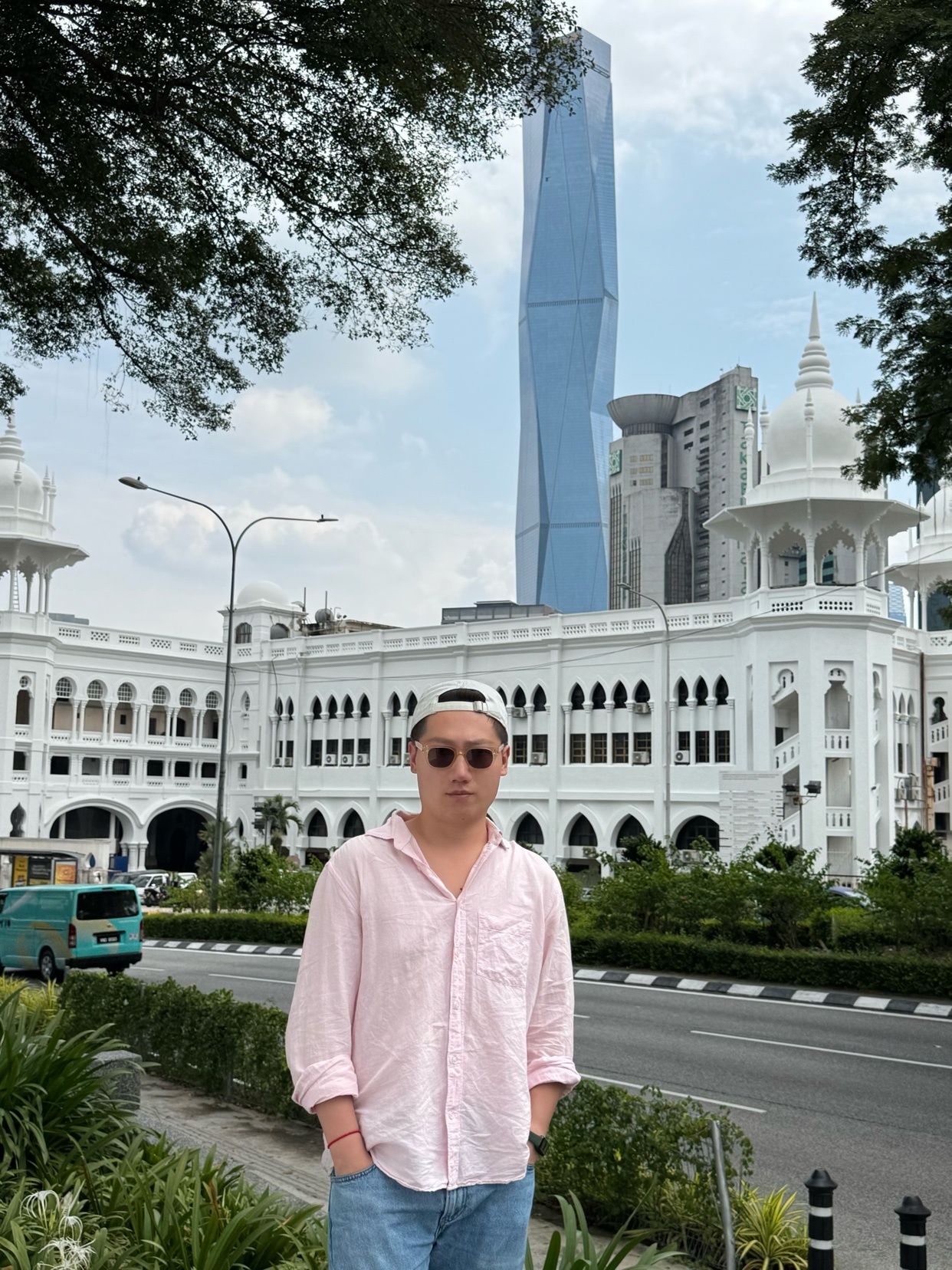 A man poses in front of a beautiful white building in Kuala Lumpur, Malaysia. The photo captures a moment of travel and urban exploration.