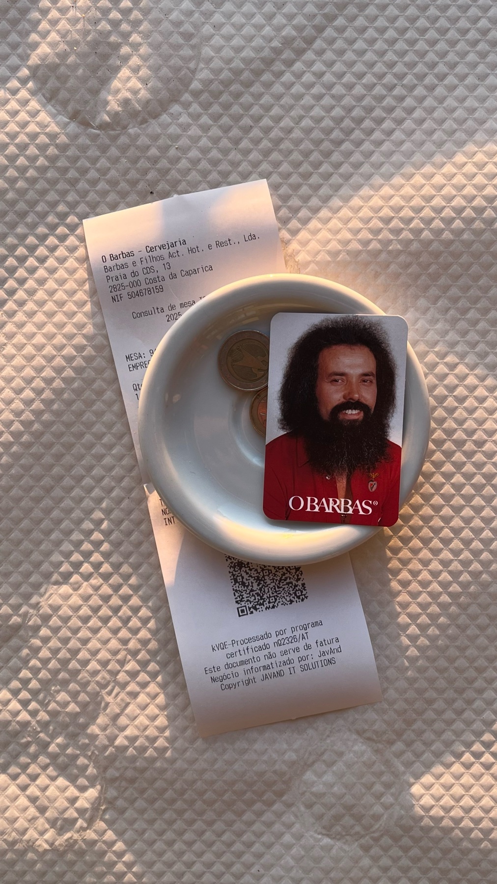 A receipt and a card with a man's photo on it are placed on a small white bowl with some coins.