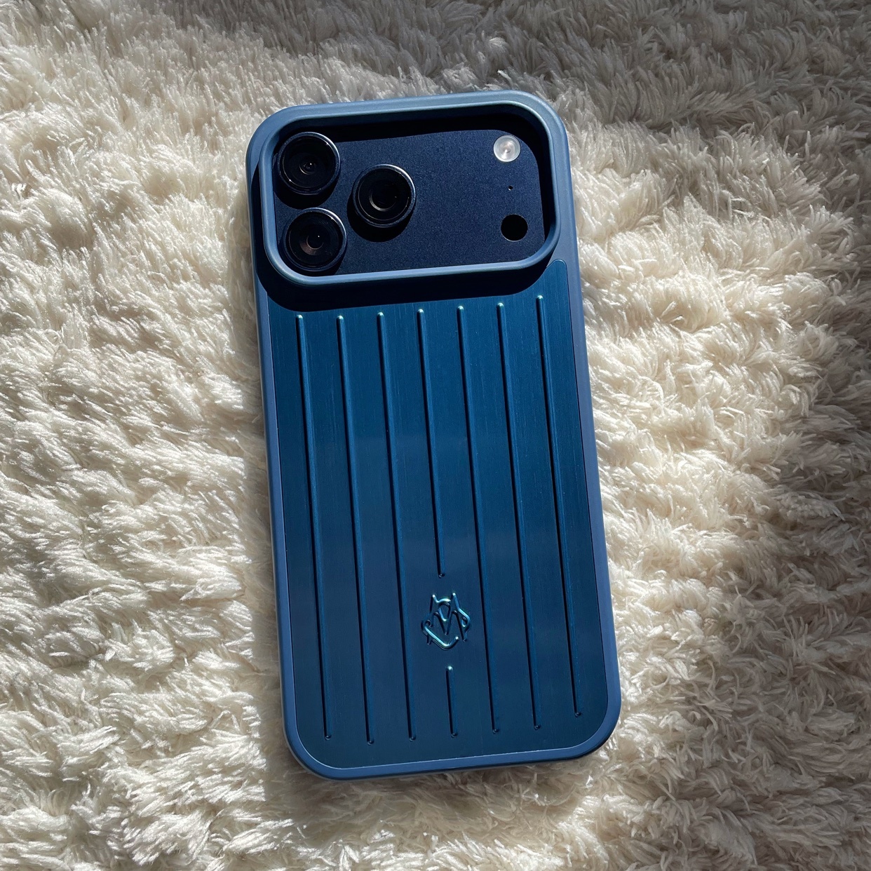 A close-up shot of a blue phone case on a white, textured surface. The case has a unique design with vertical lines.