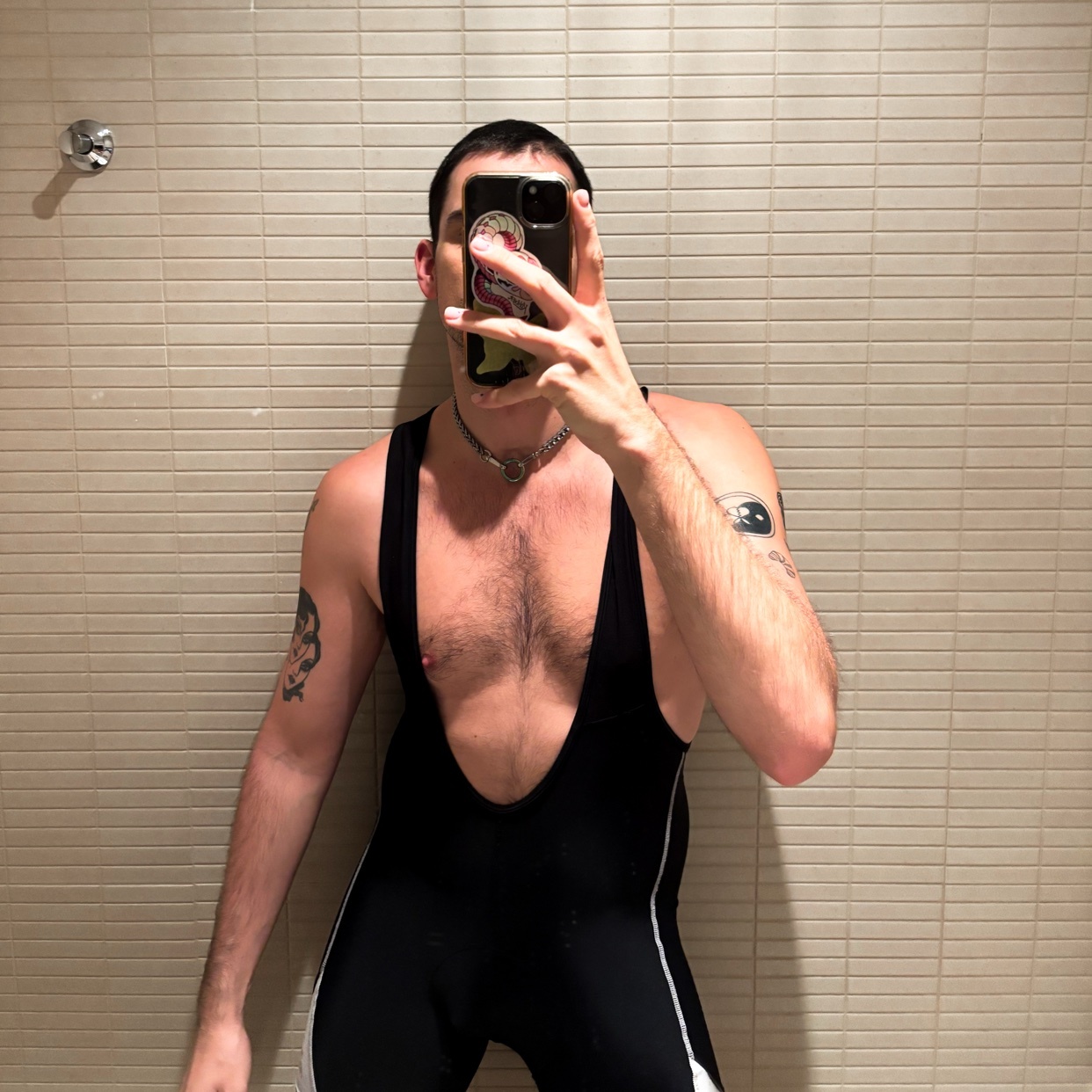 A man takes a mirror selfie, showcasing his physique. He is shirtless, wearing a black and white outfit.