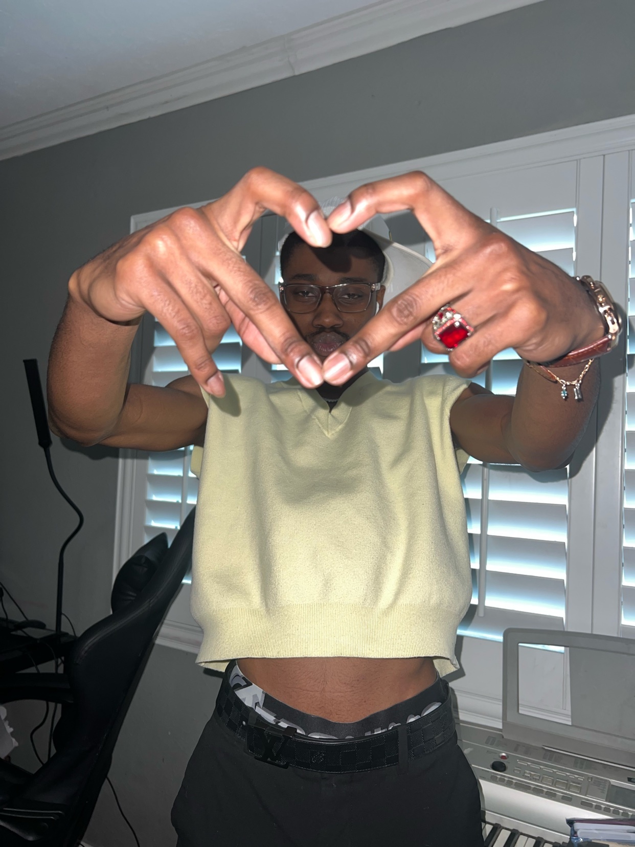 A man makes a heart shape with his hands. He is wearing a sleeveless shirt and sunglasses.