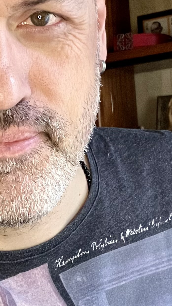 A close-up portrait of a man with a beard and grey hair. He is wearing a t-shirt.