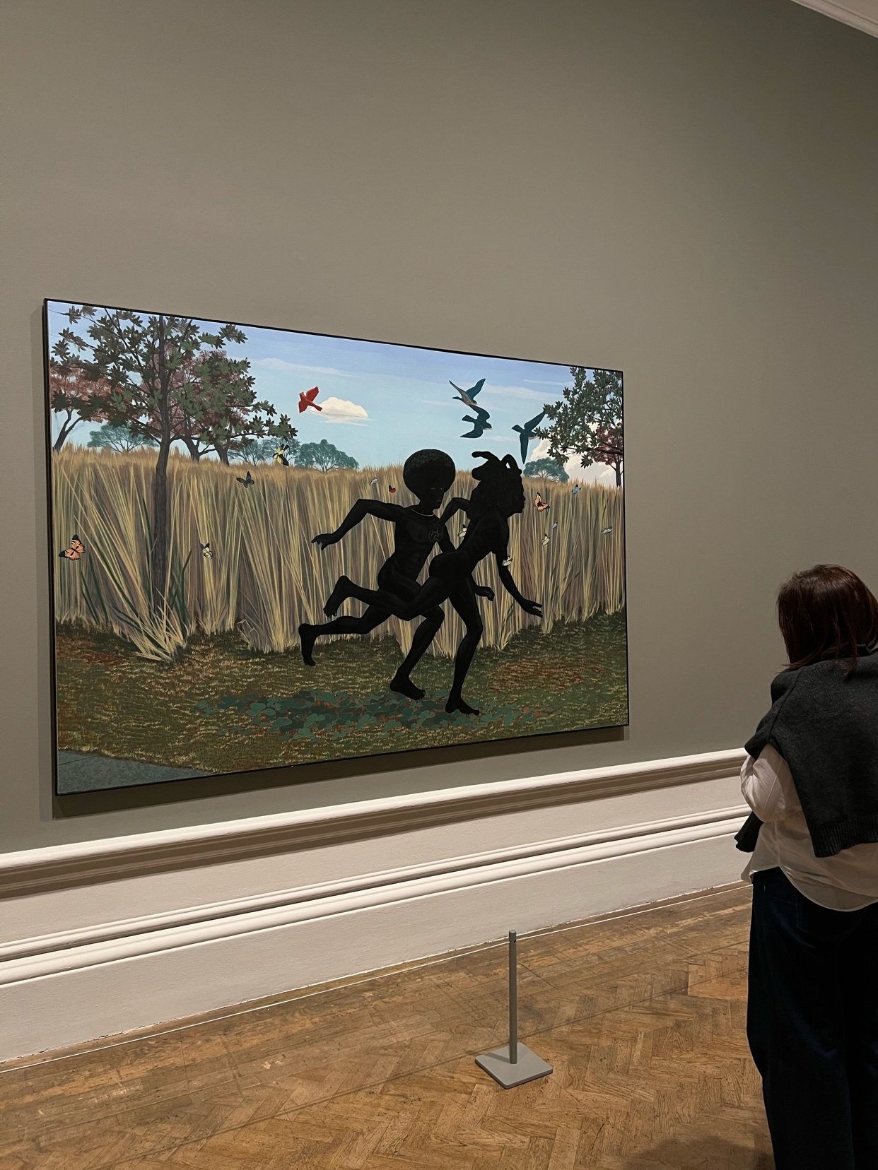 A person views a painting by Kerry James Marshall at the Royal Academy of Arts. The painting depicts two silhouetted figures running in a field.