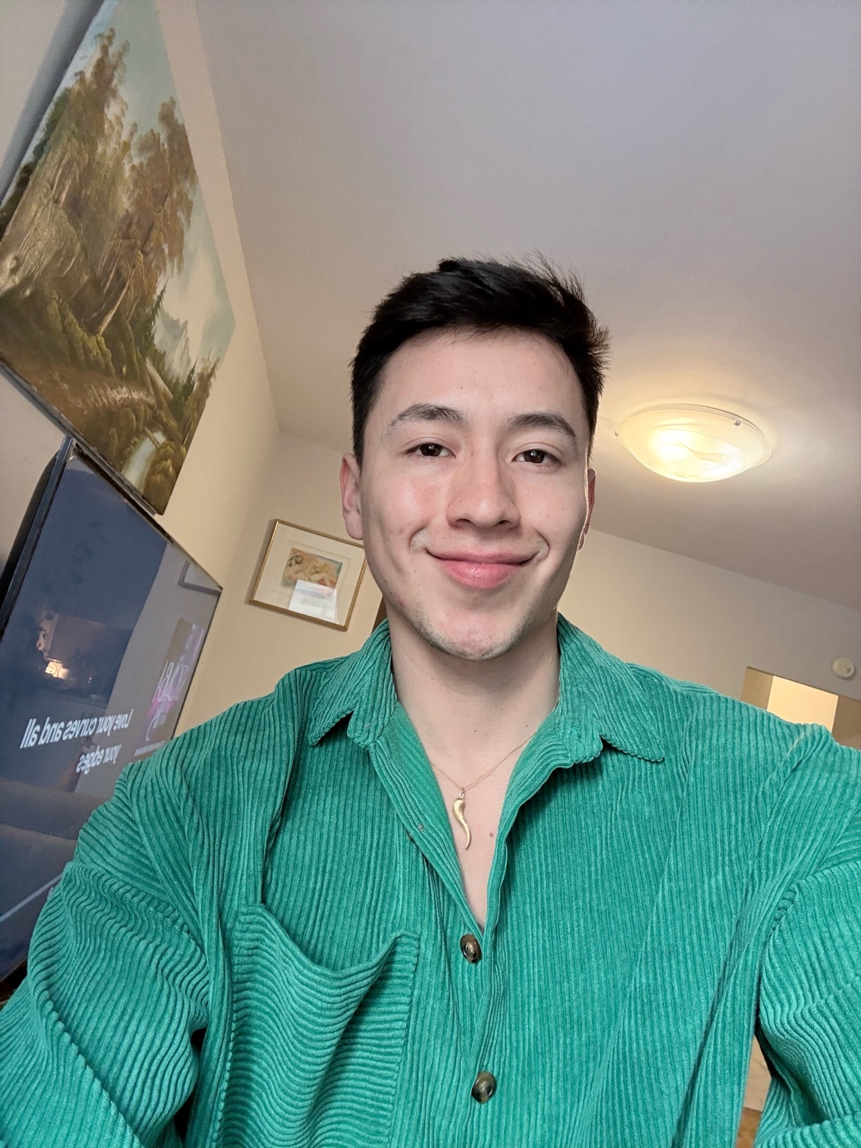 A man smiles at the camera in a selfie. He is wearing a green corduroy shirt.