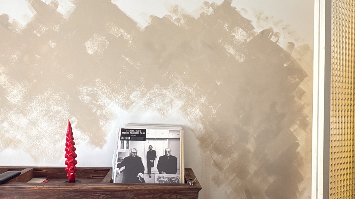 A textured wall with abstract brushstrokes in a neutral tone serves as a backdrop for a vinyl record and a red, spiral candle.