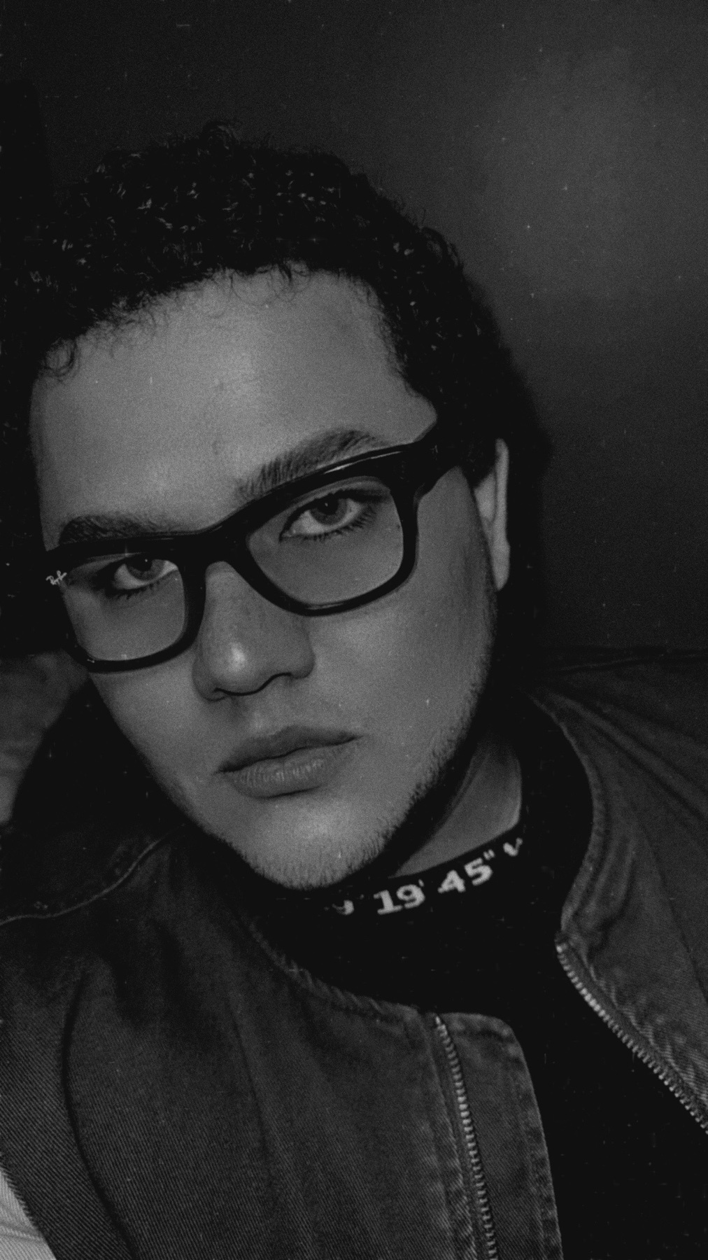 A black and white selfie of a man wearing glasses. He is looking directly at the camera with a serious expression.