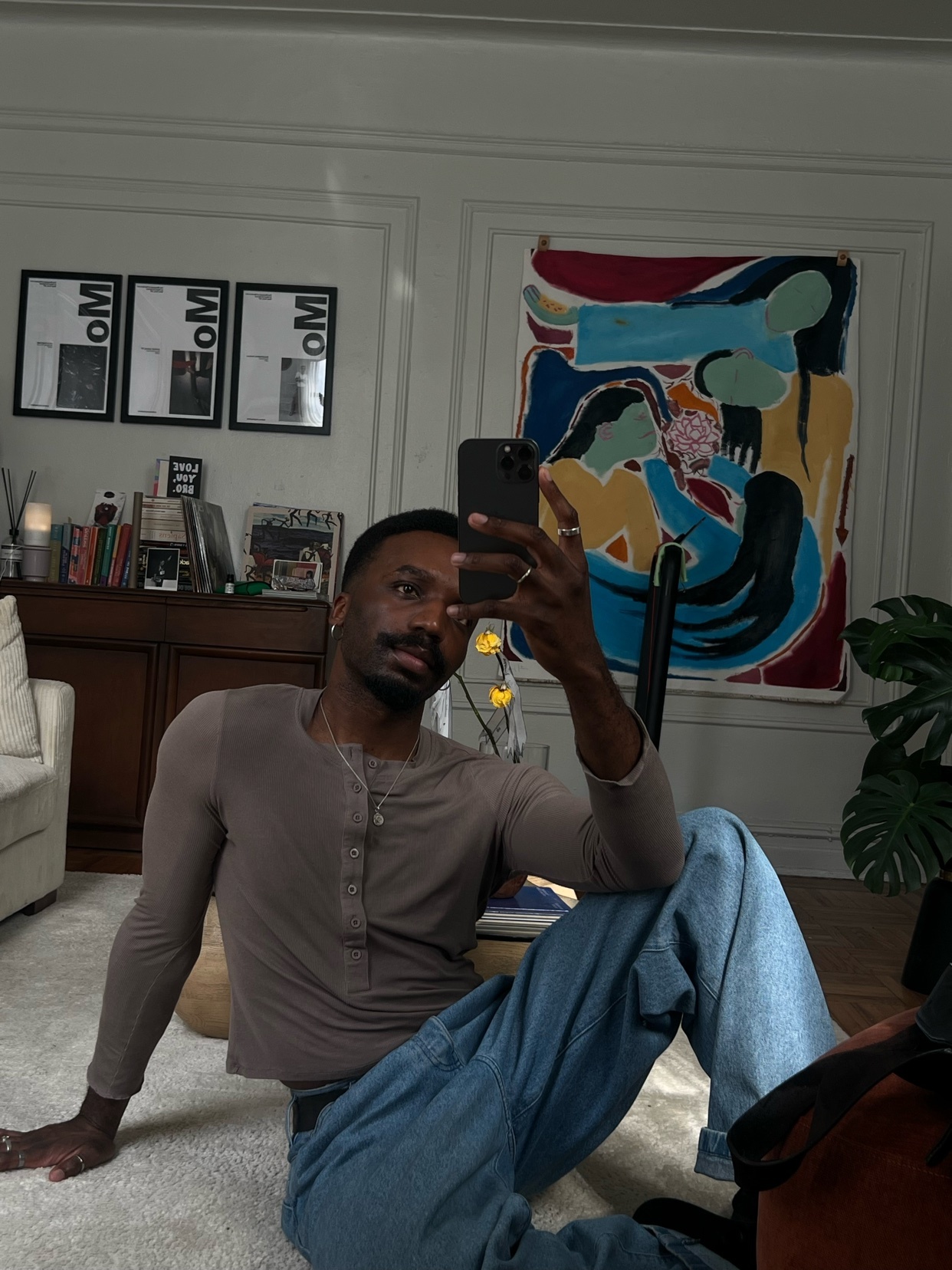 A man takes a mirror selfie in a stylish living room. The room features modern decor, including a large abstract painting and framed artwork.