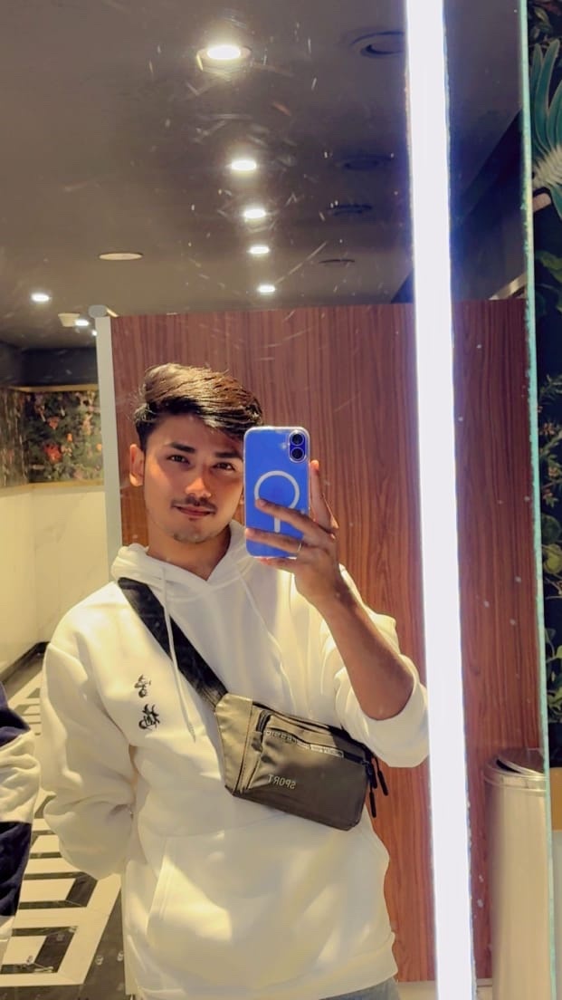 A man takes a mirror selfie, showcasing his outfit. He's wearing a white hoodie and a shoulder bag.