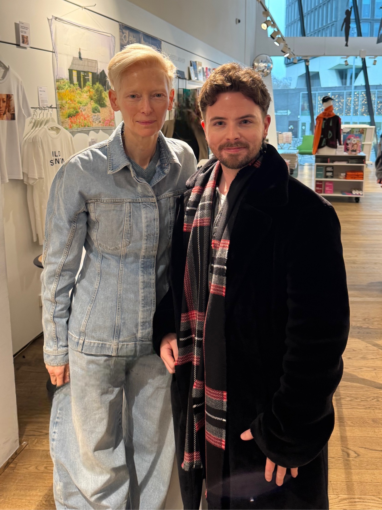 A photo of a man and a woman posing together. The woman is wearing a denim jacket and jeans, while the man is wearing a coat and scarf.
