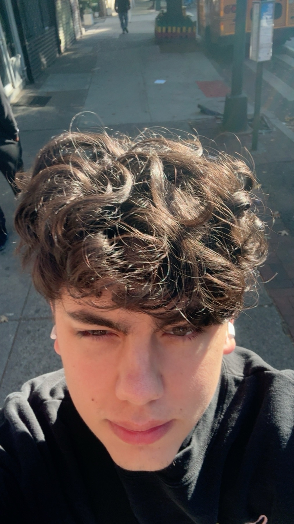A selfie of a young man with curly dark hair. He is wearing a black shirt and looking at the camera.