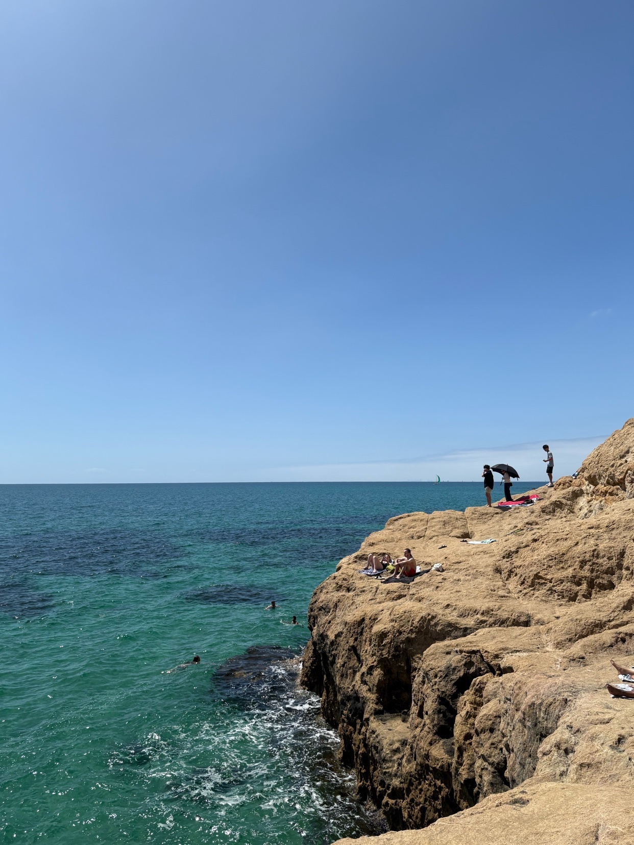 A scenic view of a beach with people enjoying the summer. The turquoise water and clear sky create a beautiful landscape.