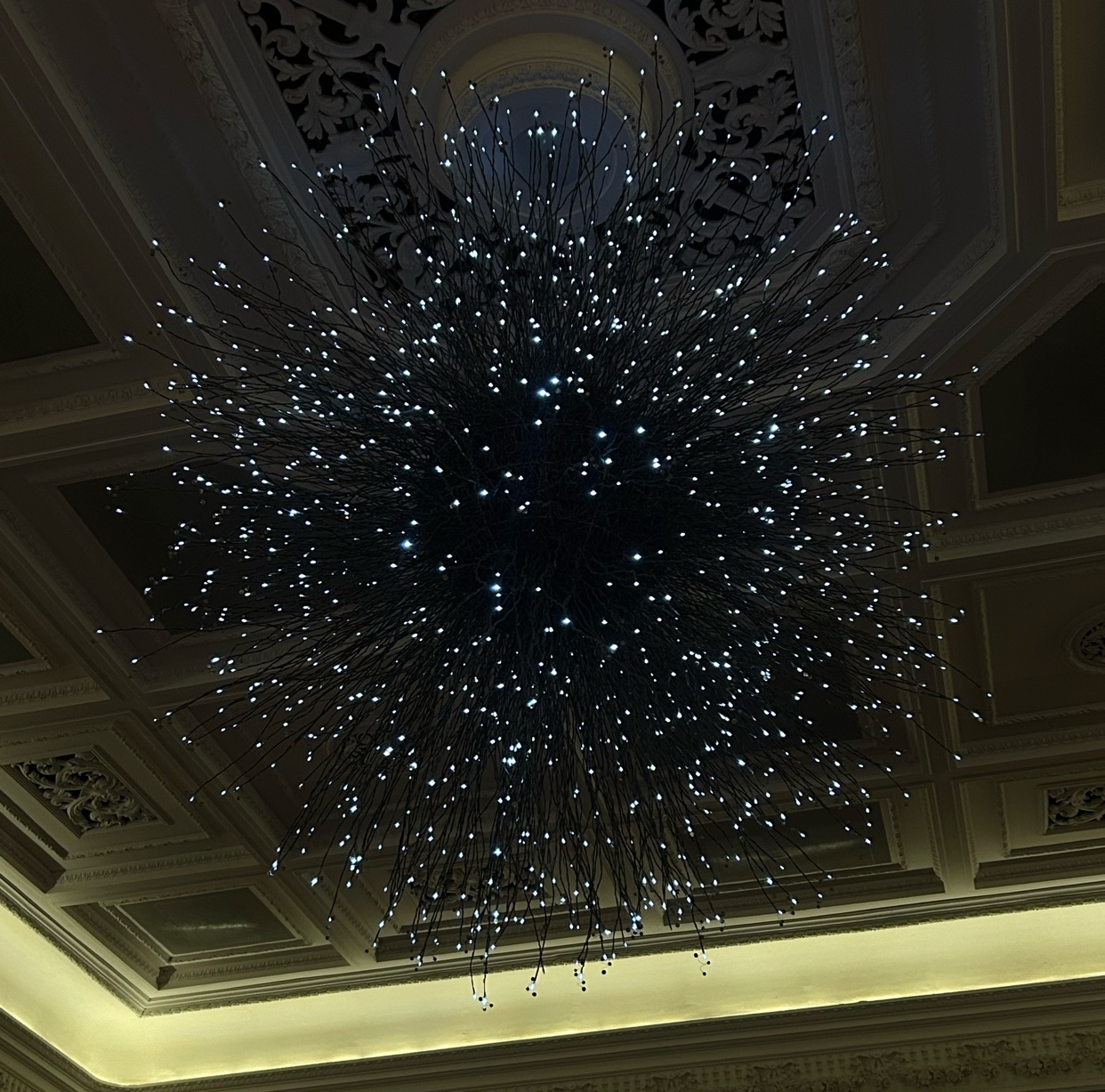 A unique, starburst-shaped chandelier hangs from a coffered ceiling, its delicate arms studded with small, bright lights.