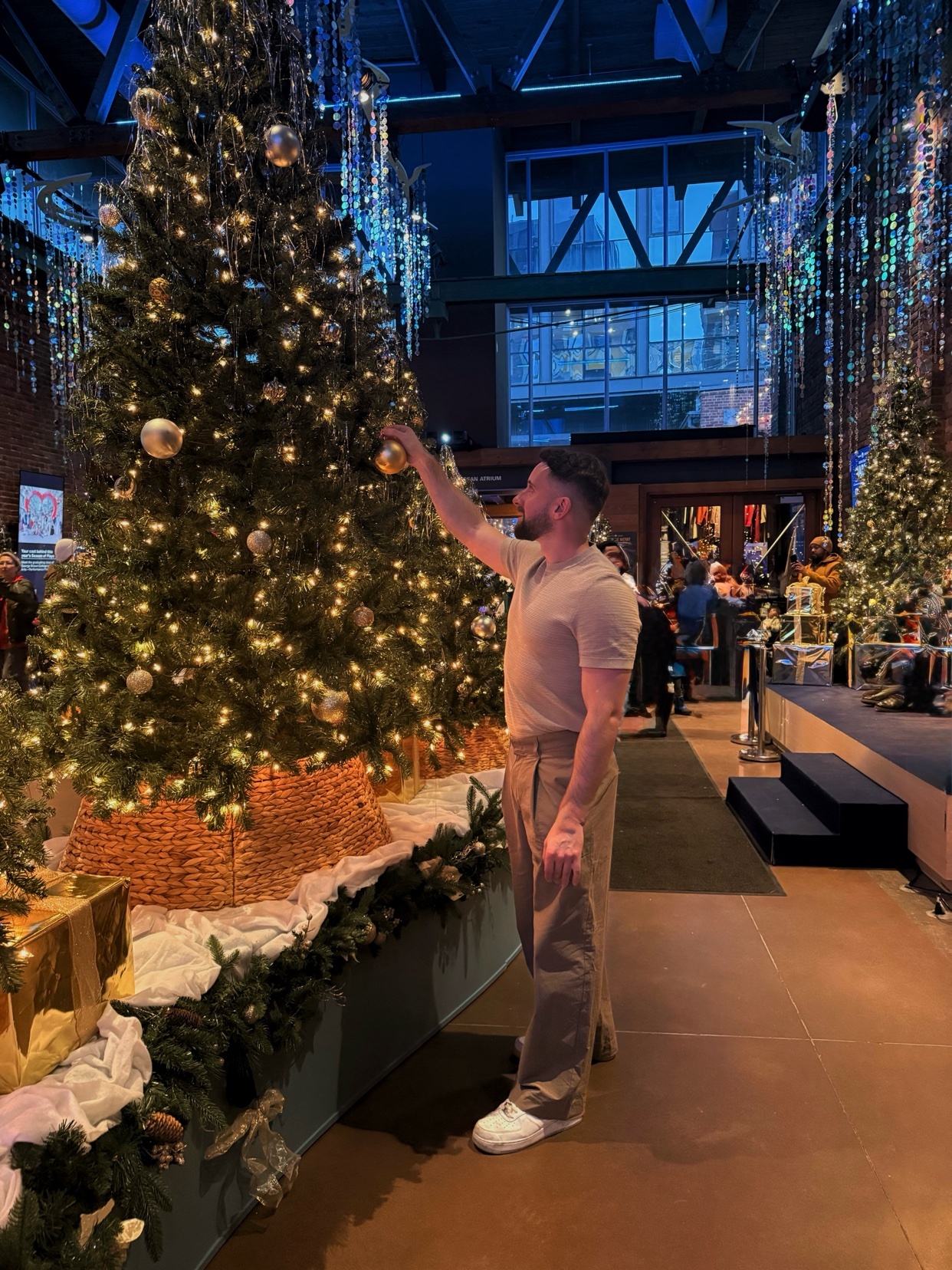 A man decorates a Christmas tree in an indoor setting. The photo captures a festive holiday scene with a focus on the man and the decorated tree.