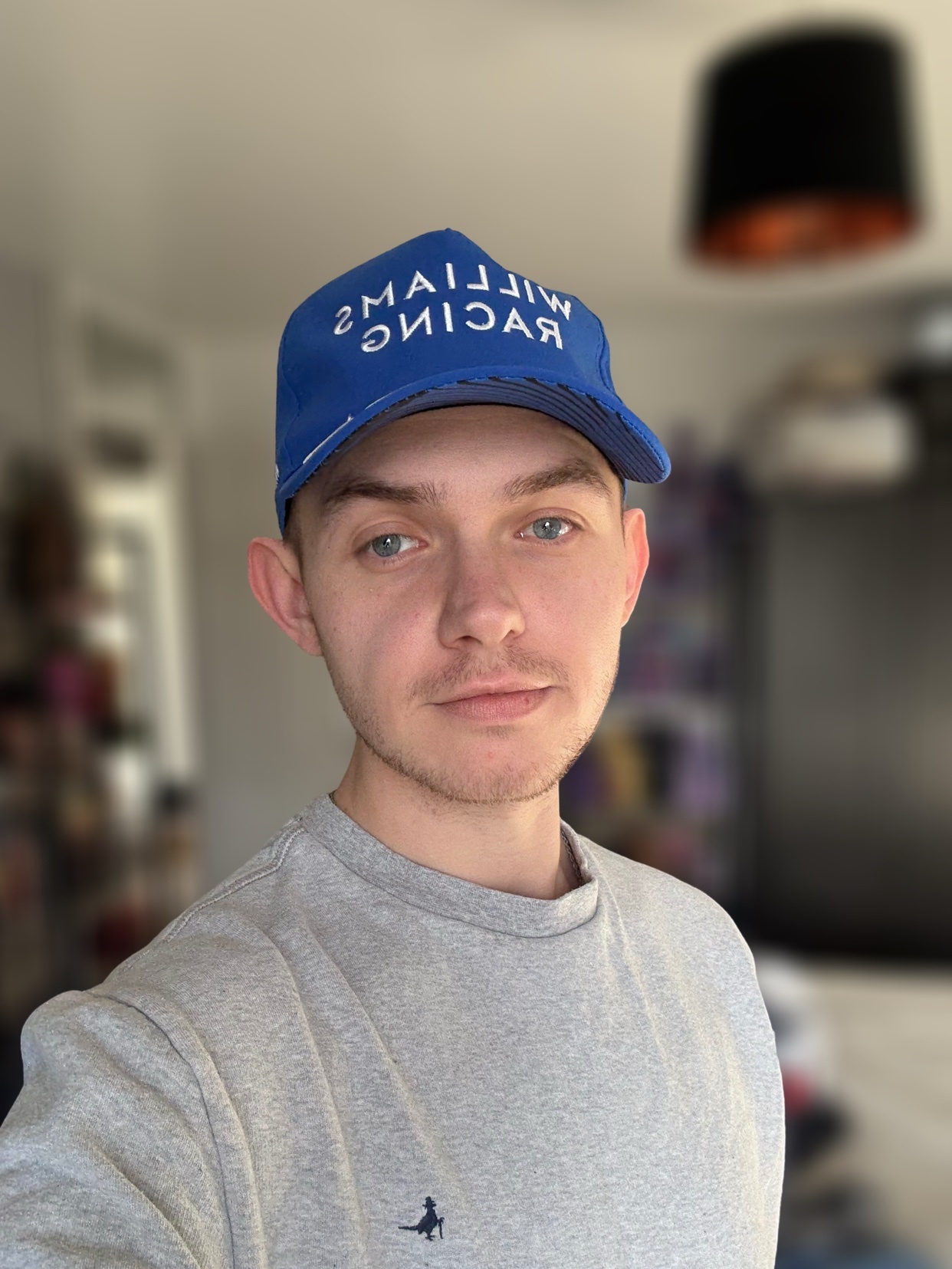 A man wearing a blue cap with white text. He is wearing a grey sweatshirt and looking at the camera.