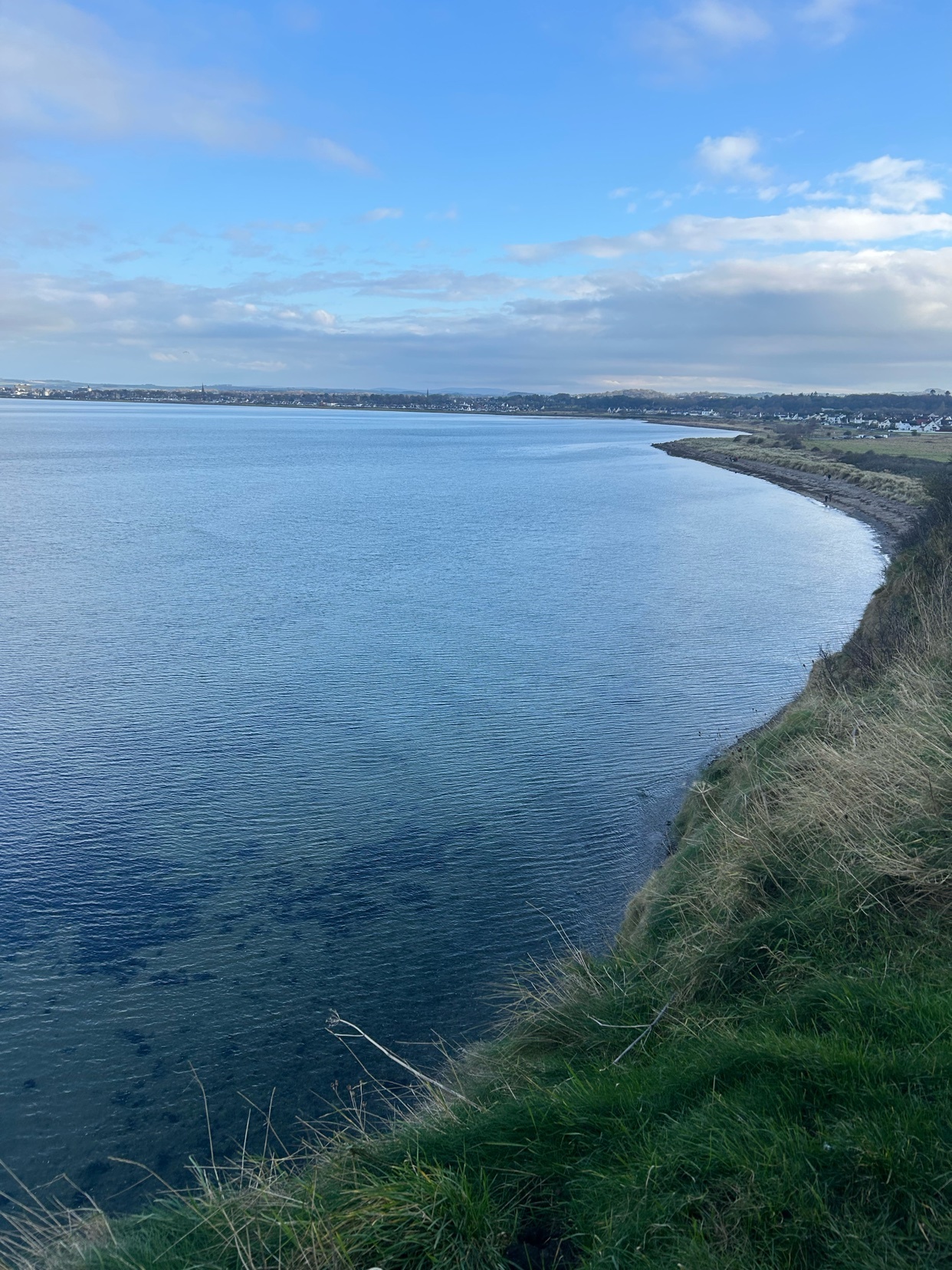 A scenic view of a coastline with a body of water under a blue sky. The image captures the natural beauty of the landscape.