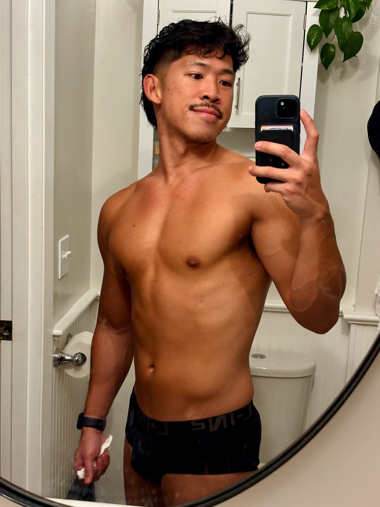 A man takes a mirror selfie in his bathroom, showcasing his muscular physique. He is shirtless and wearing underwear.