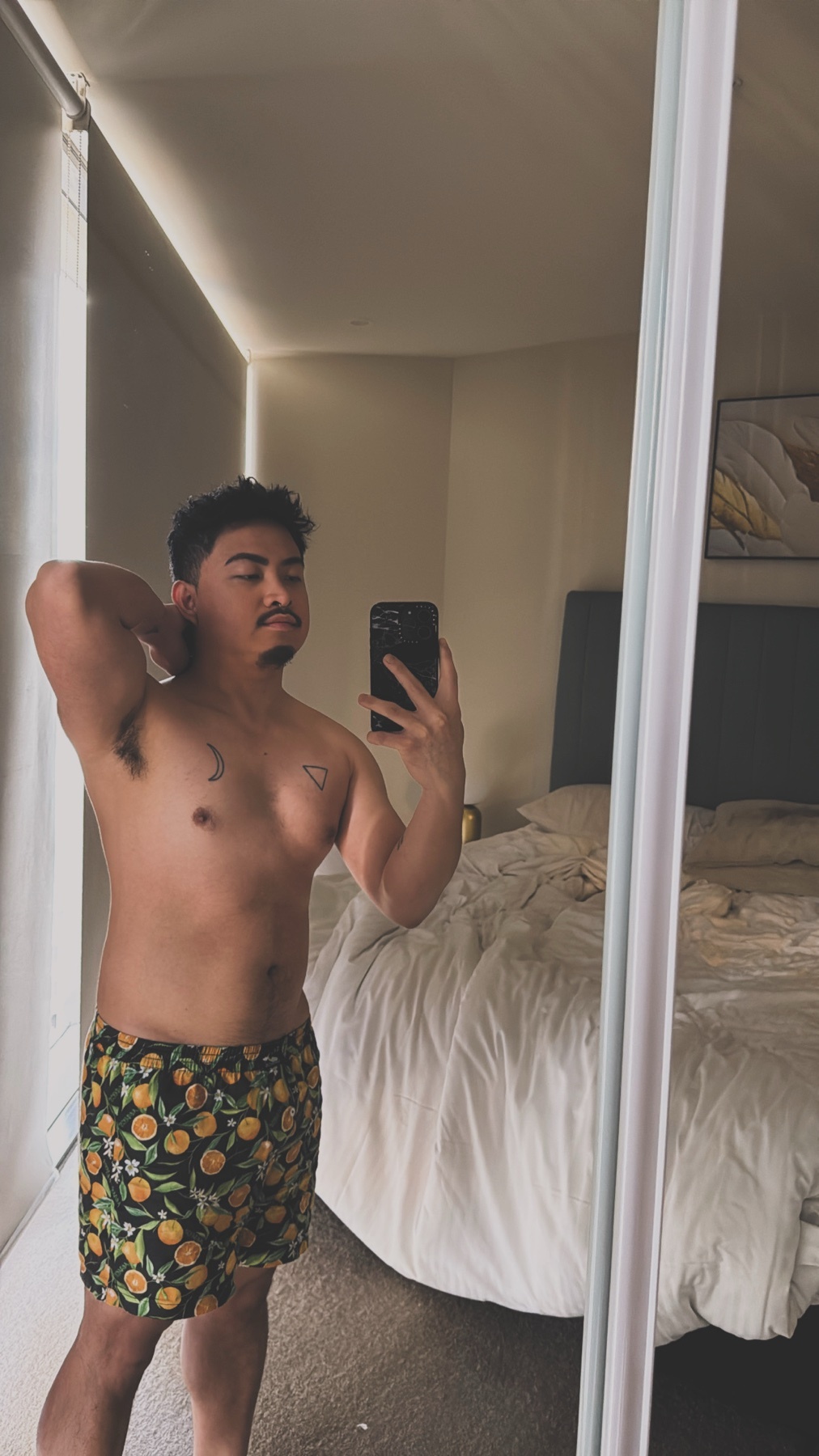 A man in patterned boxer briefs poses for a mirror selfie in a bedroom.