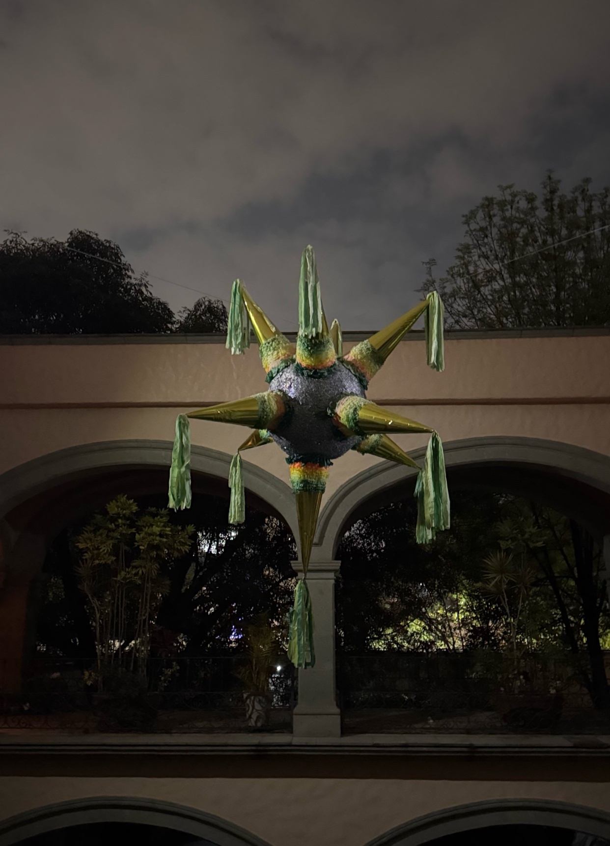 A star-shaped pinata hangs in front of an arched building at night. The pinata is a festive decoration, likely for a party or celebration.