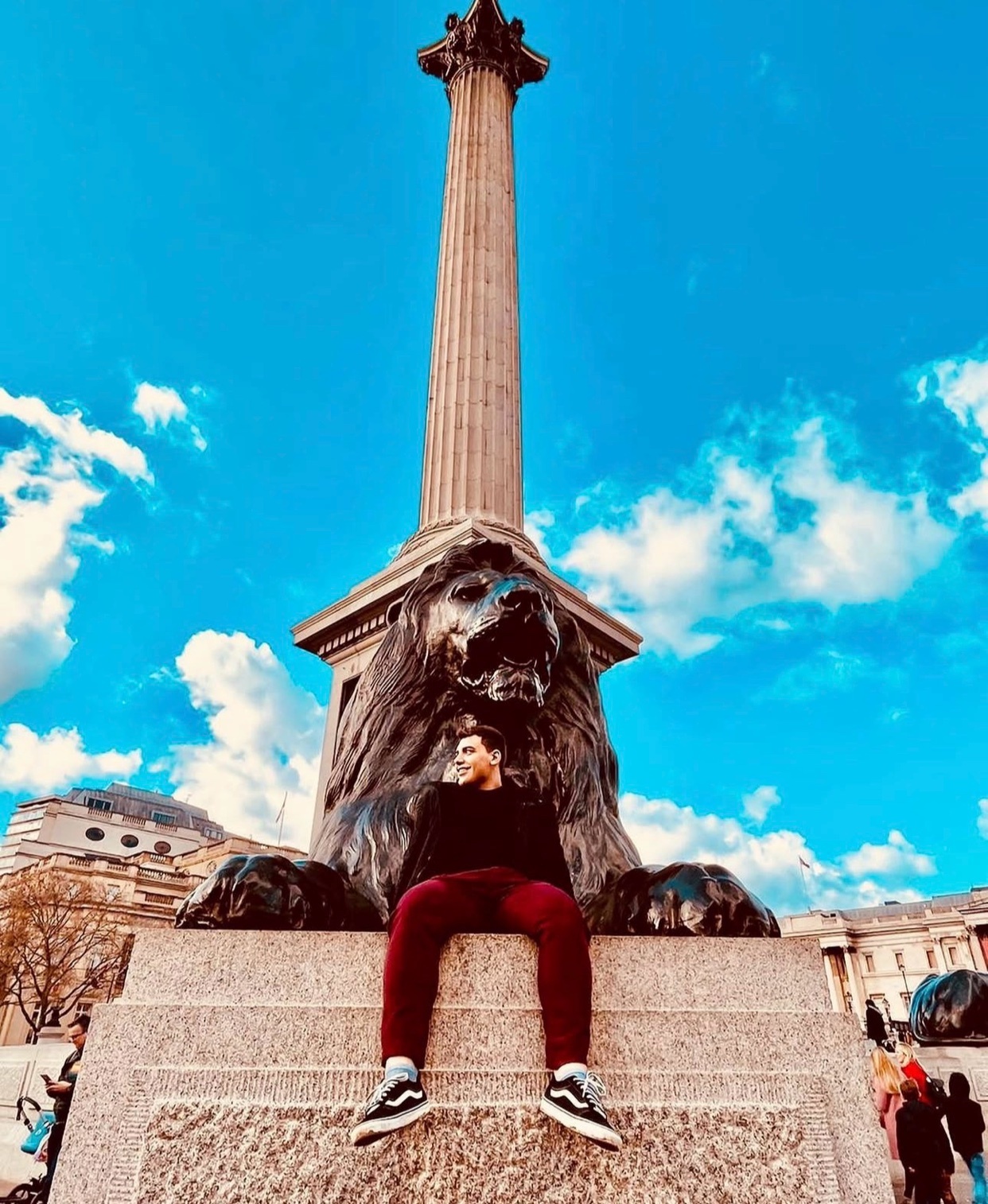 A man poses in front of Nelson's Column in Trafalgar Square, London. The photo captures a moment of travel and urban exploration.