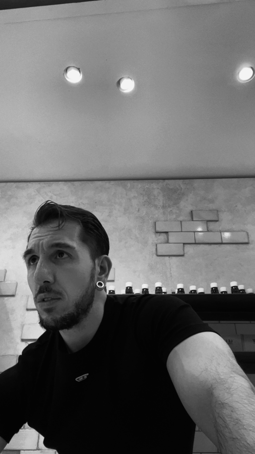 A black and white photo of a man looking up. He is wearing a black t-shirt and has a beard.