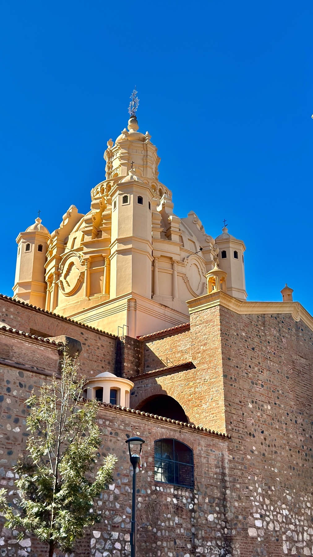 A majestic yellow-domed church with a stone facade stands tall against a clear blue sky. The intricate architectural details of the building are highlighted by the bright sunlight.