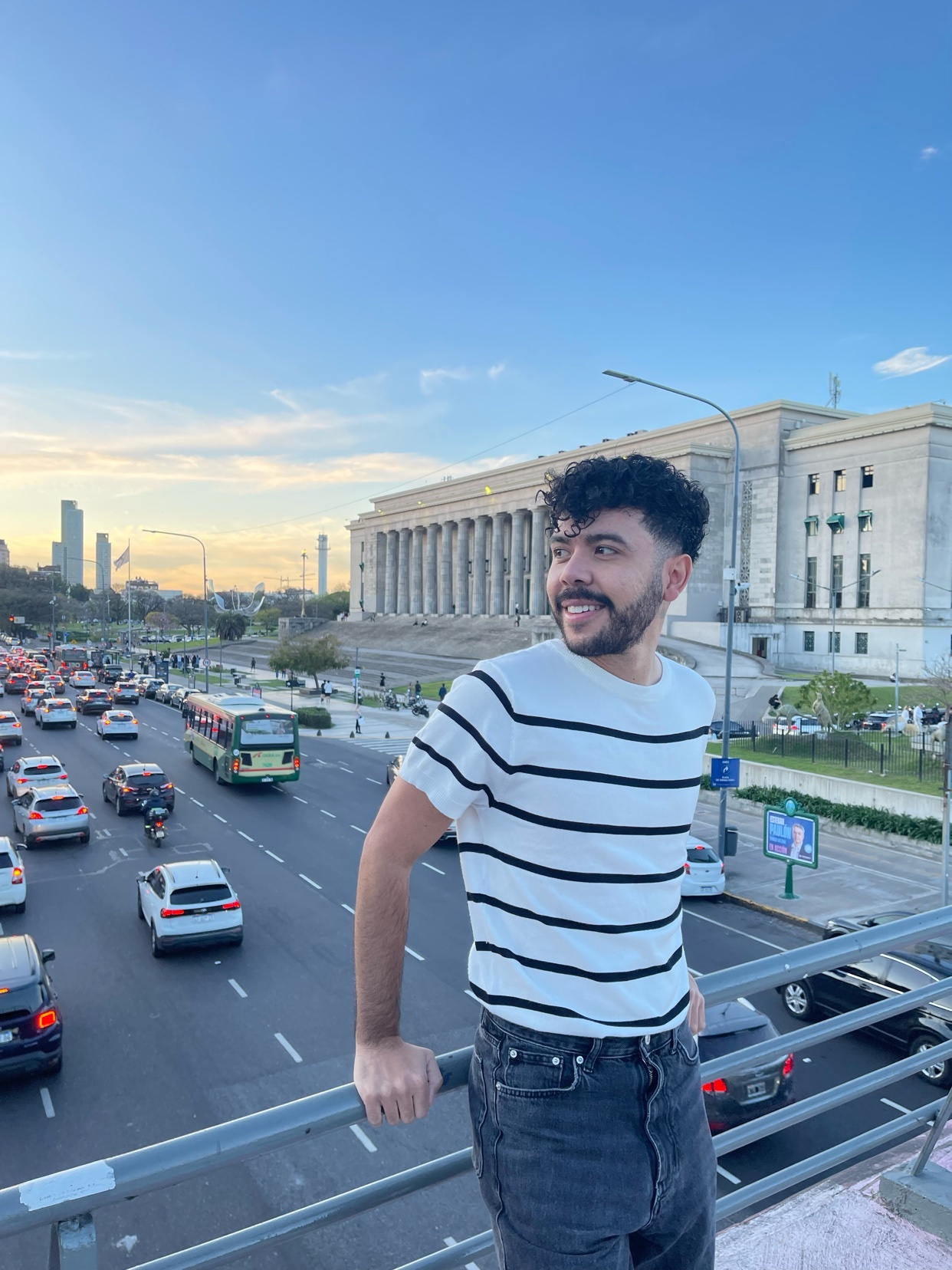 A man poses on a bridge overlooking a busy street in Buenos Aires, Argentina. The photo captures a cityscape with a modern aesthetic.