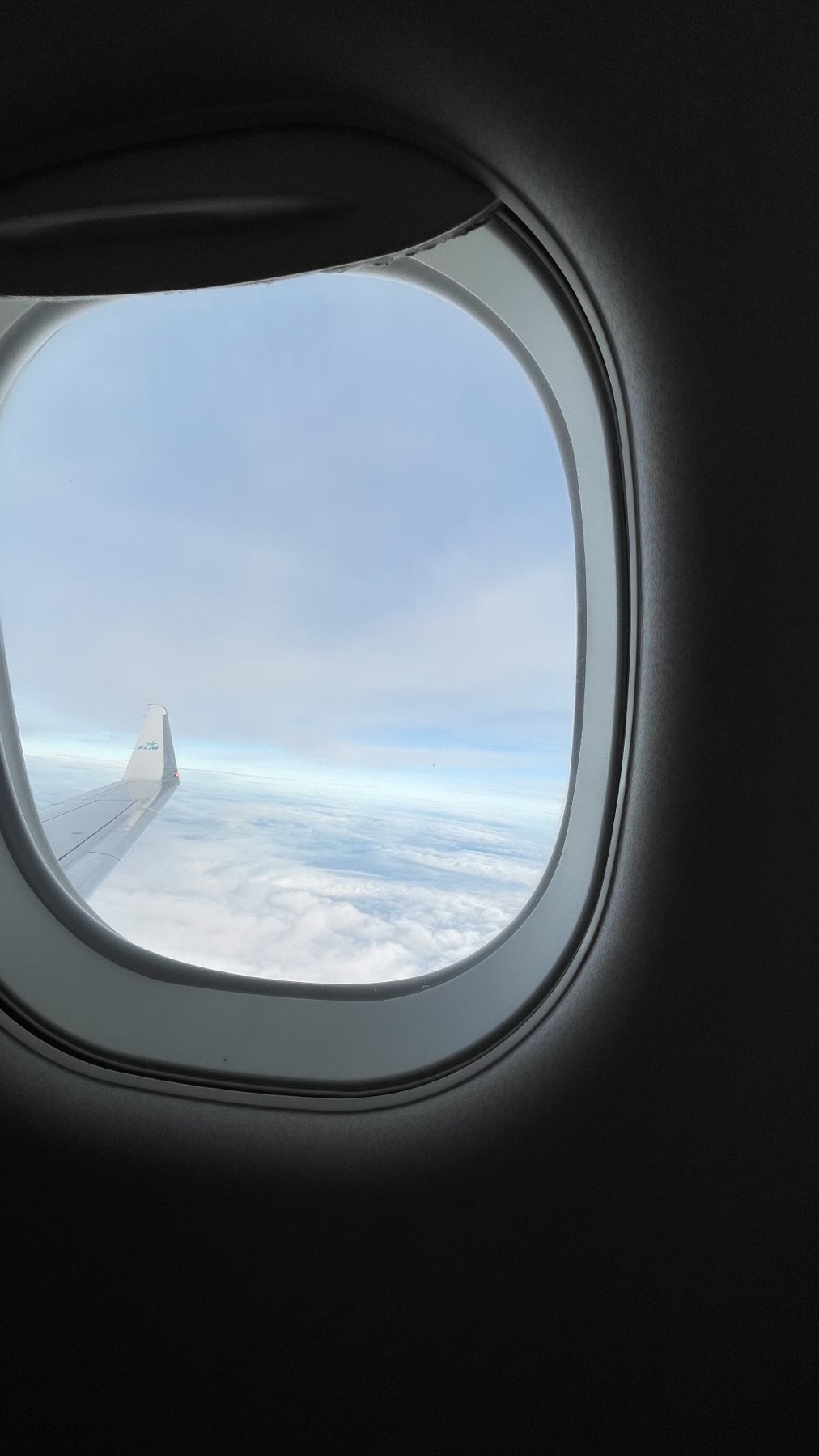 A view from an airplane window, showcasing the sky and clouds. The airplane wing is visible, adding to the sense of flight and travel.