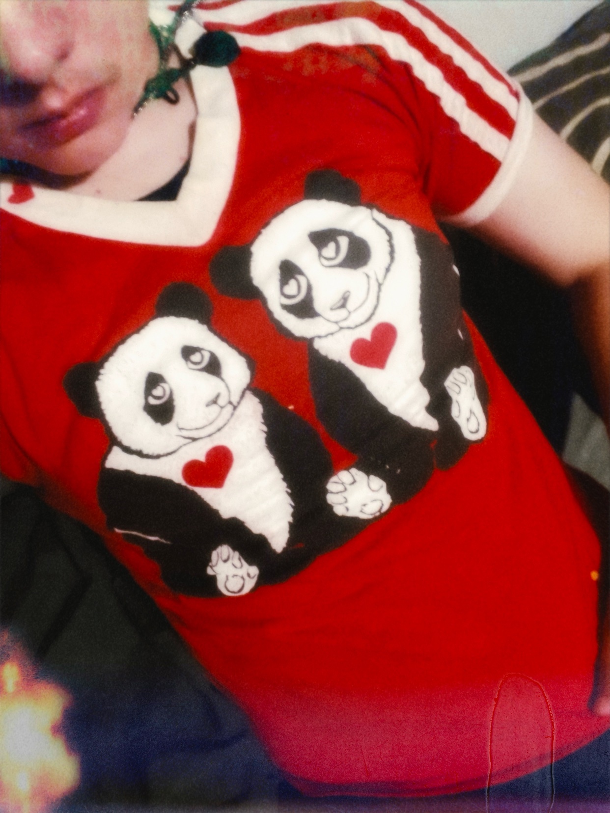 A close-up shot of a person wearing a red t-shirt with two pandas and red hearts printed on it. The person's face is partially visible, and they are wearing a necklace.